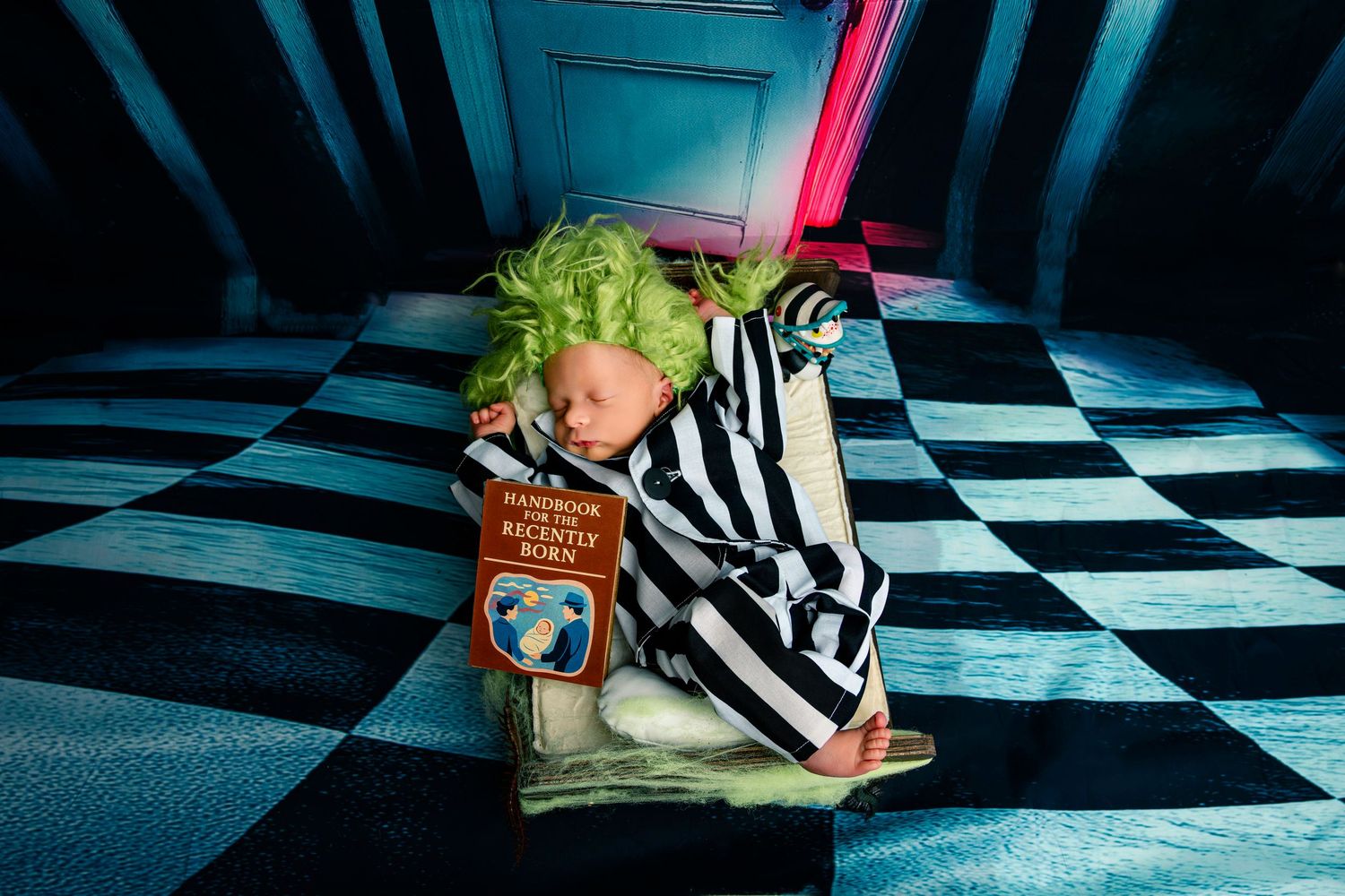 Newborn baby dressed as Beetlejuice with green hair wig and black-and-white striped outfit on checkered floor.