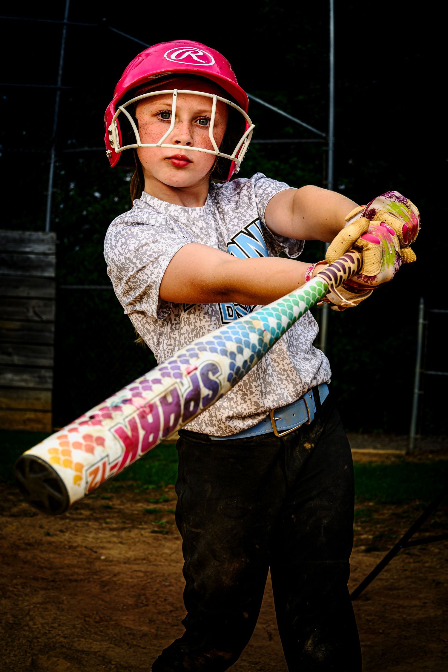 Young softball player in pink helmet swings colorful Spark bat at practice field.