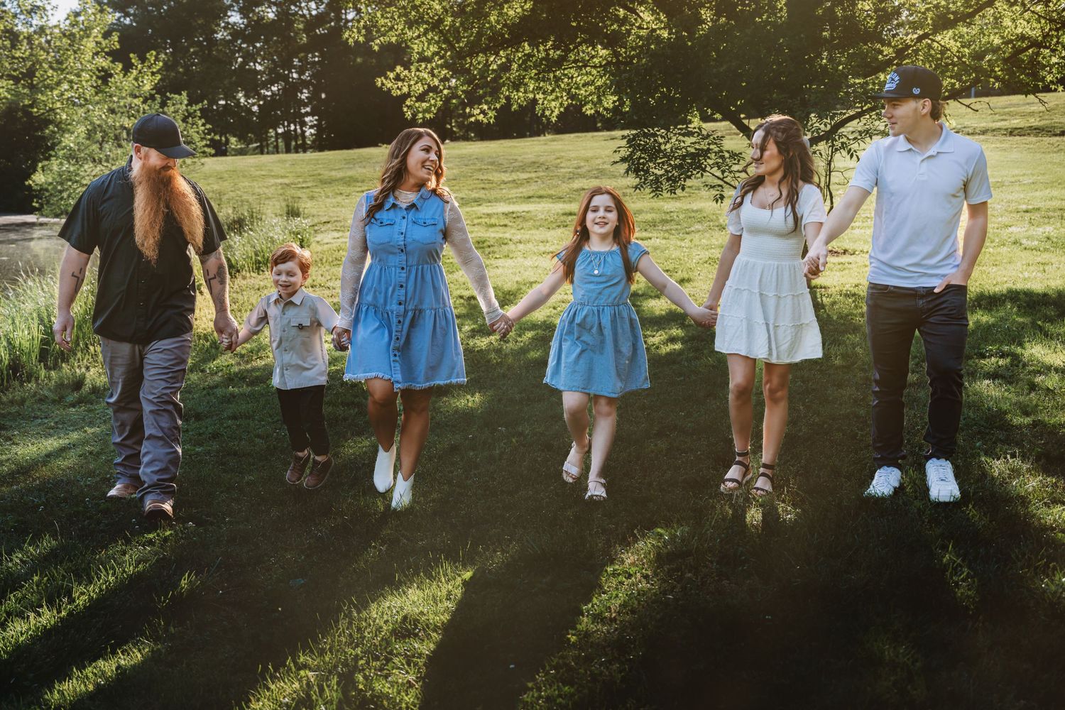 Family of six holding hands walking through a sunny green park, smiling and dressed in coordinated blue and white outfits.