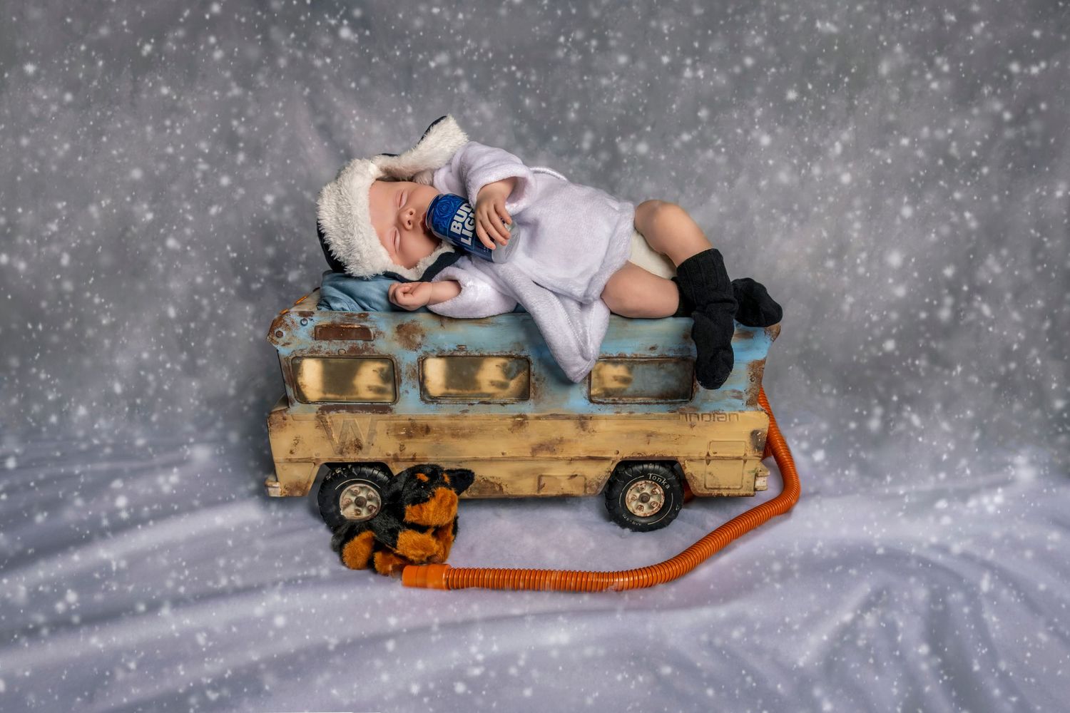 Newborn baby sleeping on a vintage toy truck with a winter hat, surrounded by a snowy backdrop. Christmas vacation newborn photo