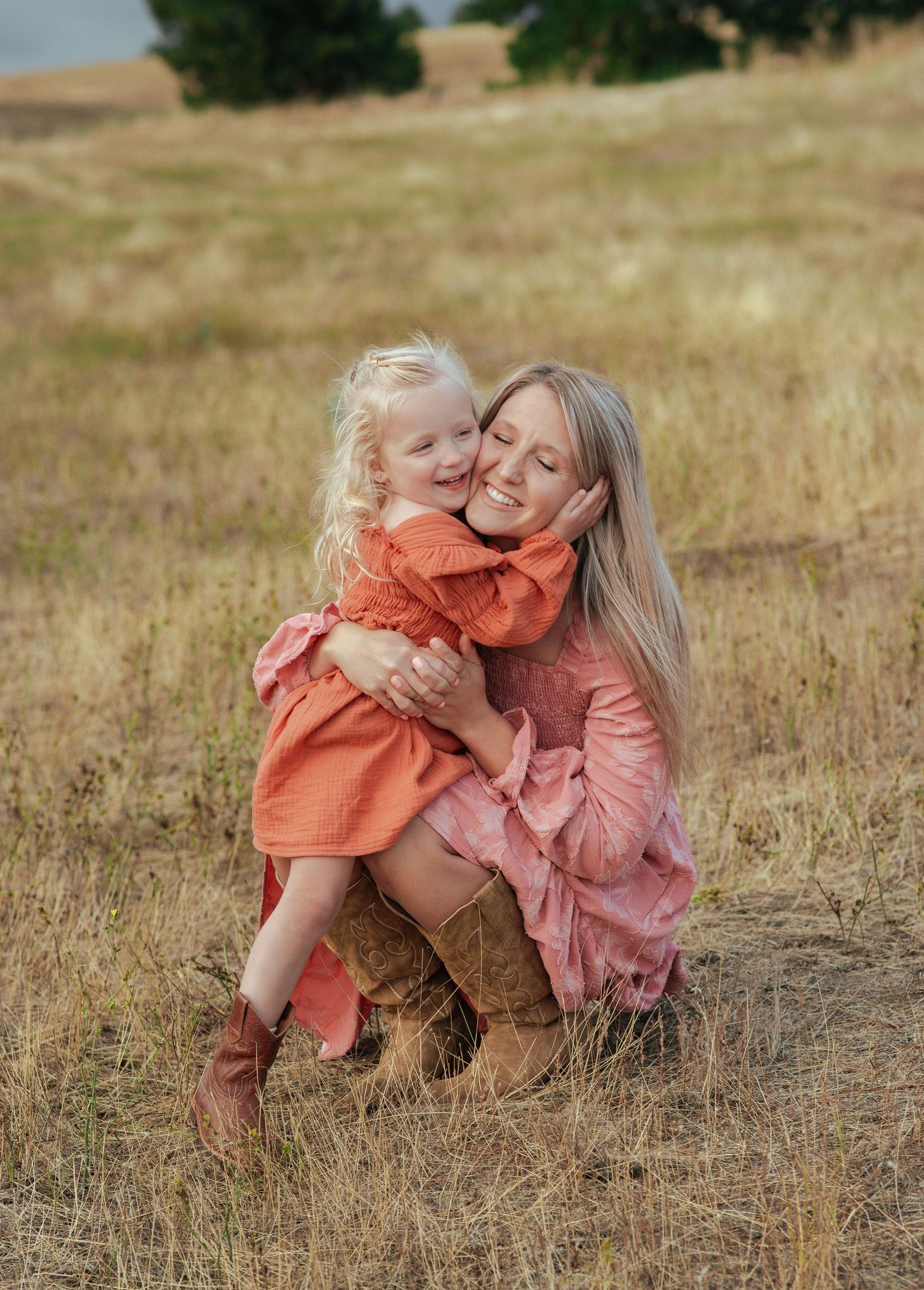 Mother and toddler daughter in orange dresses share sweet hug in golden grass field.