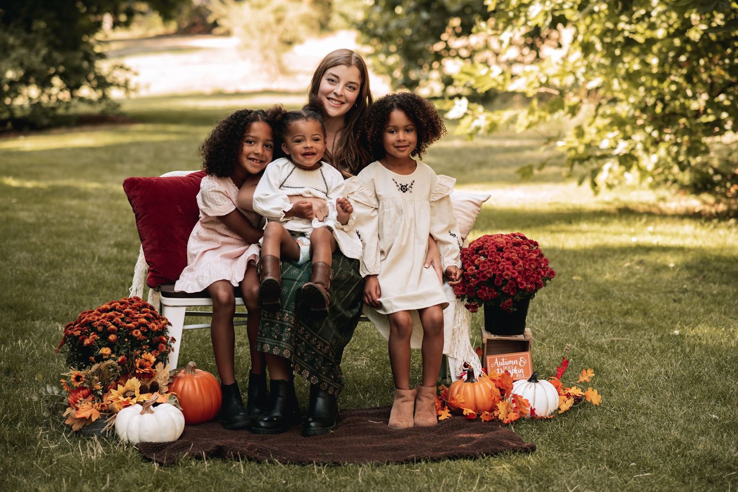 Woman with three children in fall outdoor portrait with pumpkins and autumn flowers.