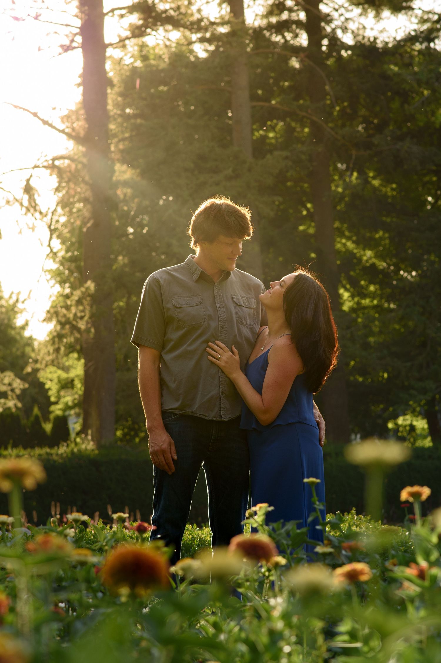 Couple sharing romantic moment in flower garden with golden sunlight backdrop.