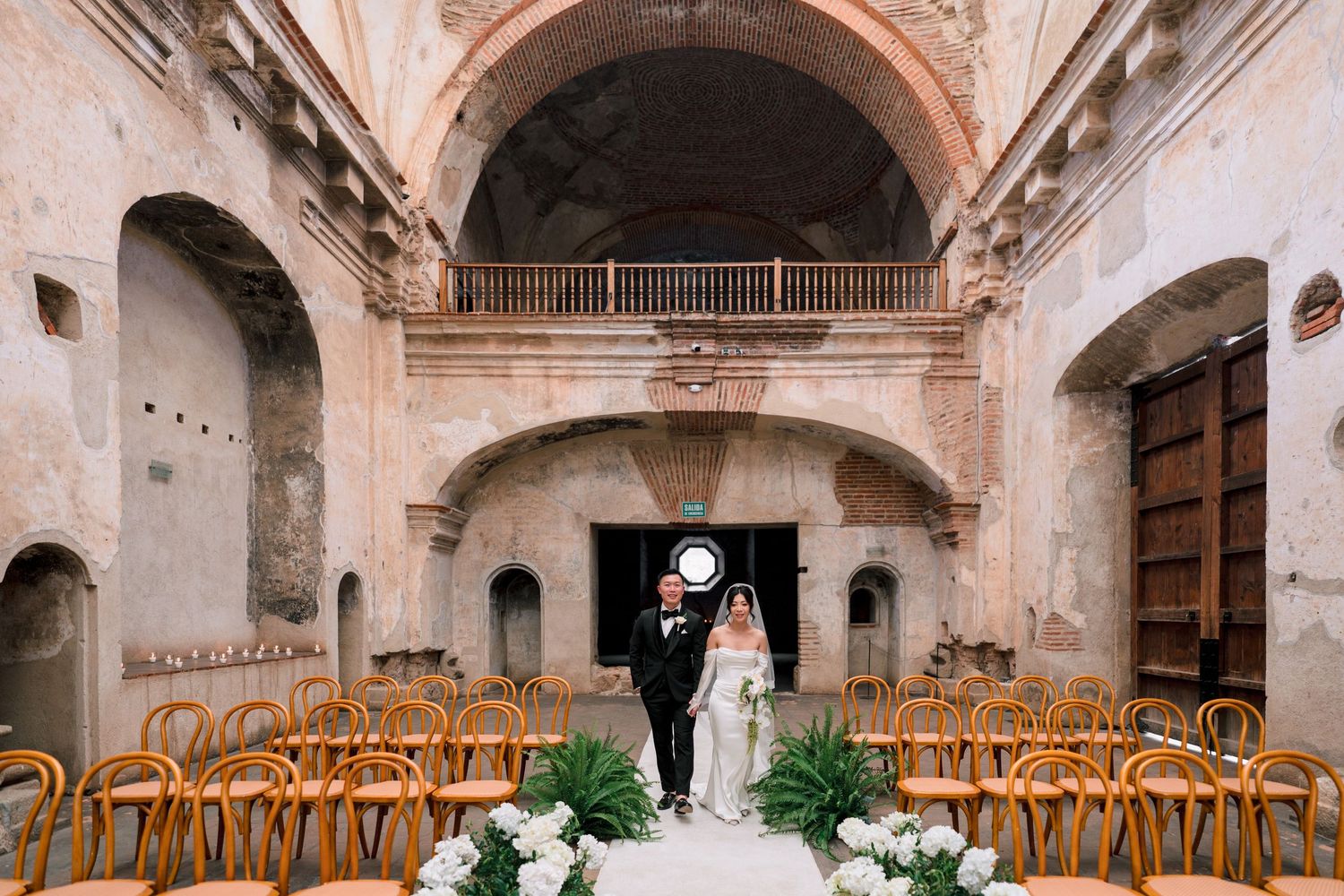 Bride and groom at altar in stunning rustic chapel with arched ceilings and wooden chairs.