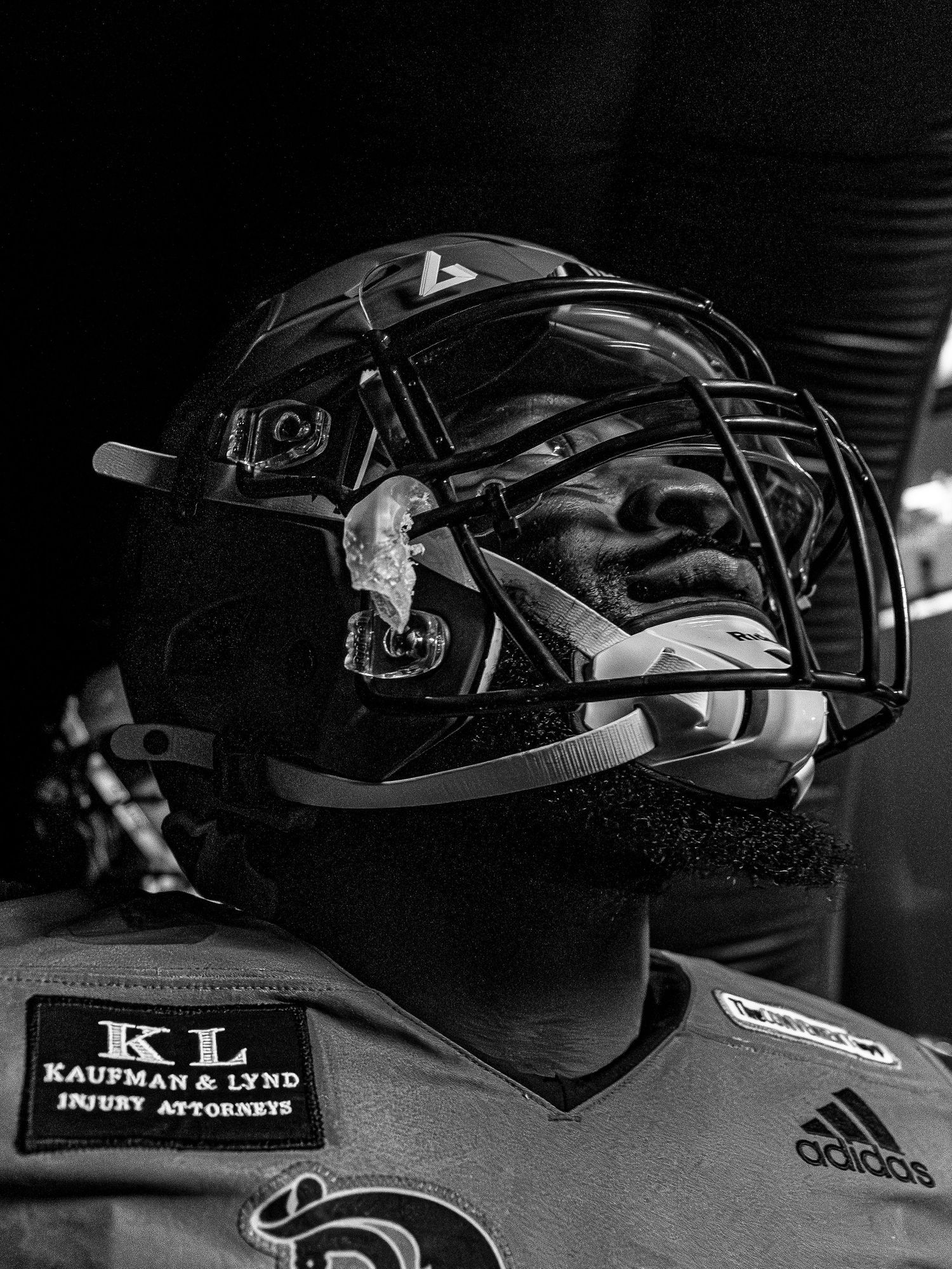 Black and white photo of a football player wearing a helmet with face guard and Kaufman & Lynd sponsor patch.