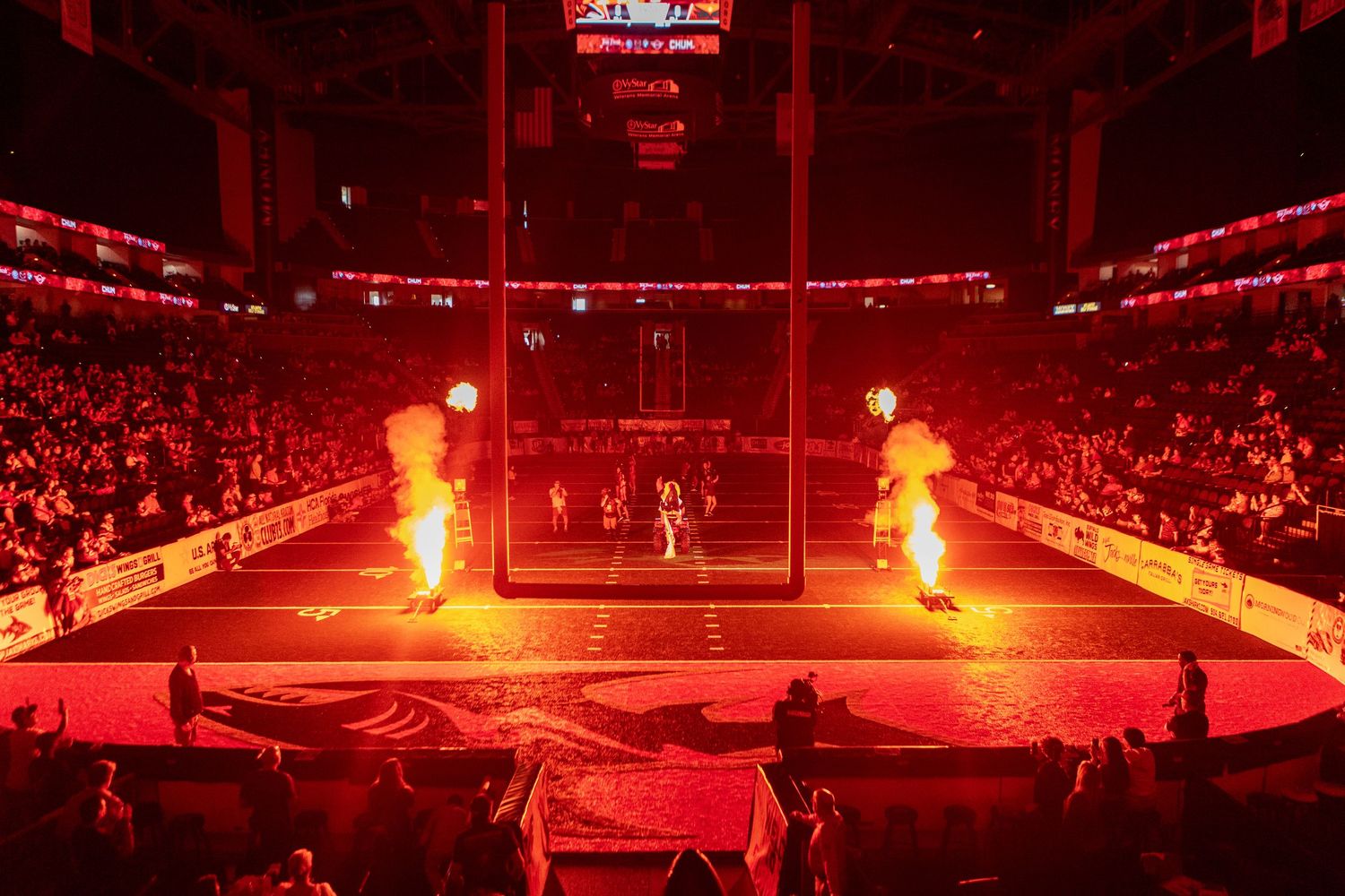 Hockey arena illuminated with dramatic red lighting and pyrotechnics during a pre-game show.