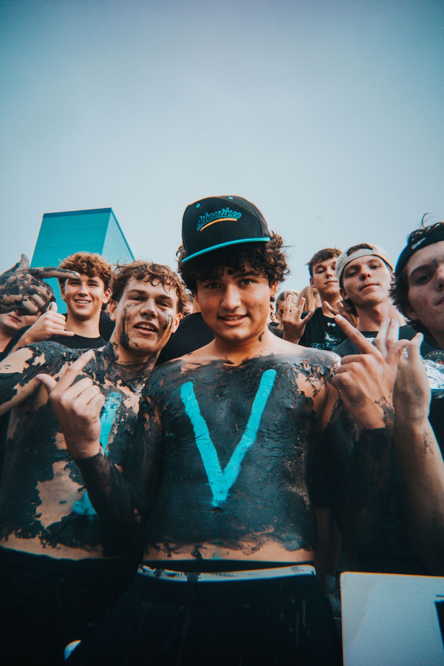 Excited crowd of shirtless fans cheering with teal lighting effects.