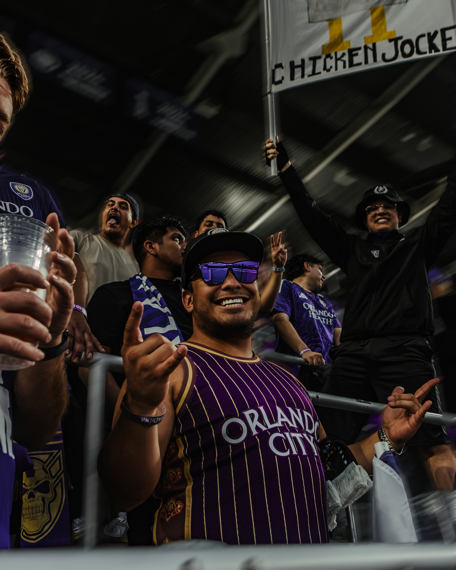 Enthusiastic sports fans in purple striped jerseys cheer in a dimly lit venue.