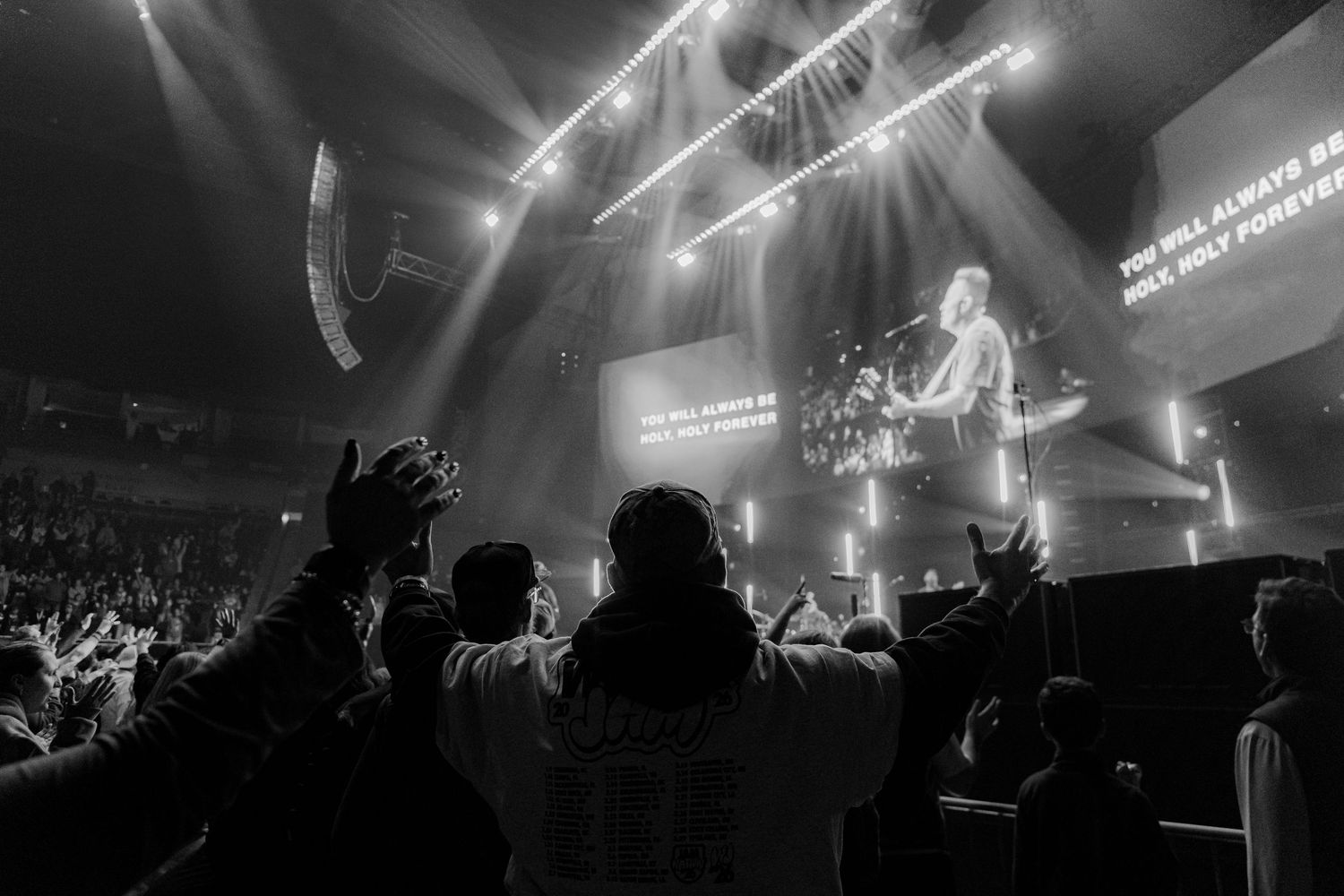 Concert venue filled with silhouettes of crowd against bright stage lighting.