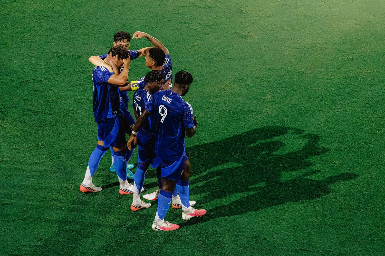 France football players in blue jerseys celebrating a goal together on a green pitch during a match.