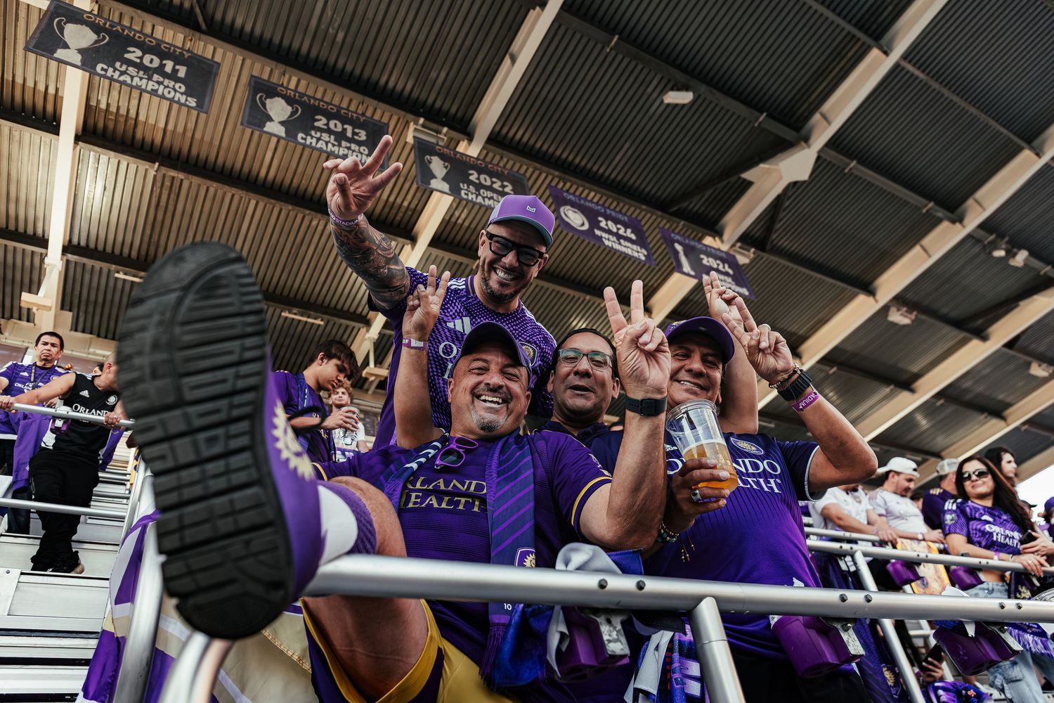 Enthusiastic fans in purple team colors celebrating at a sports venue.