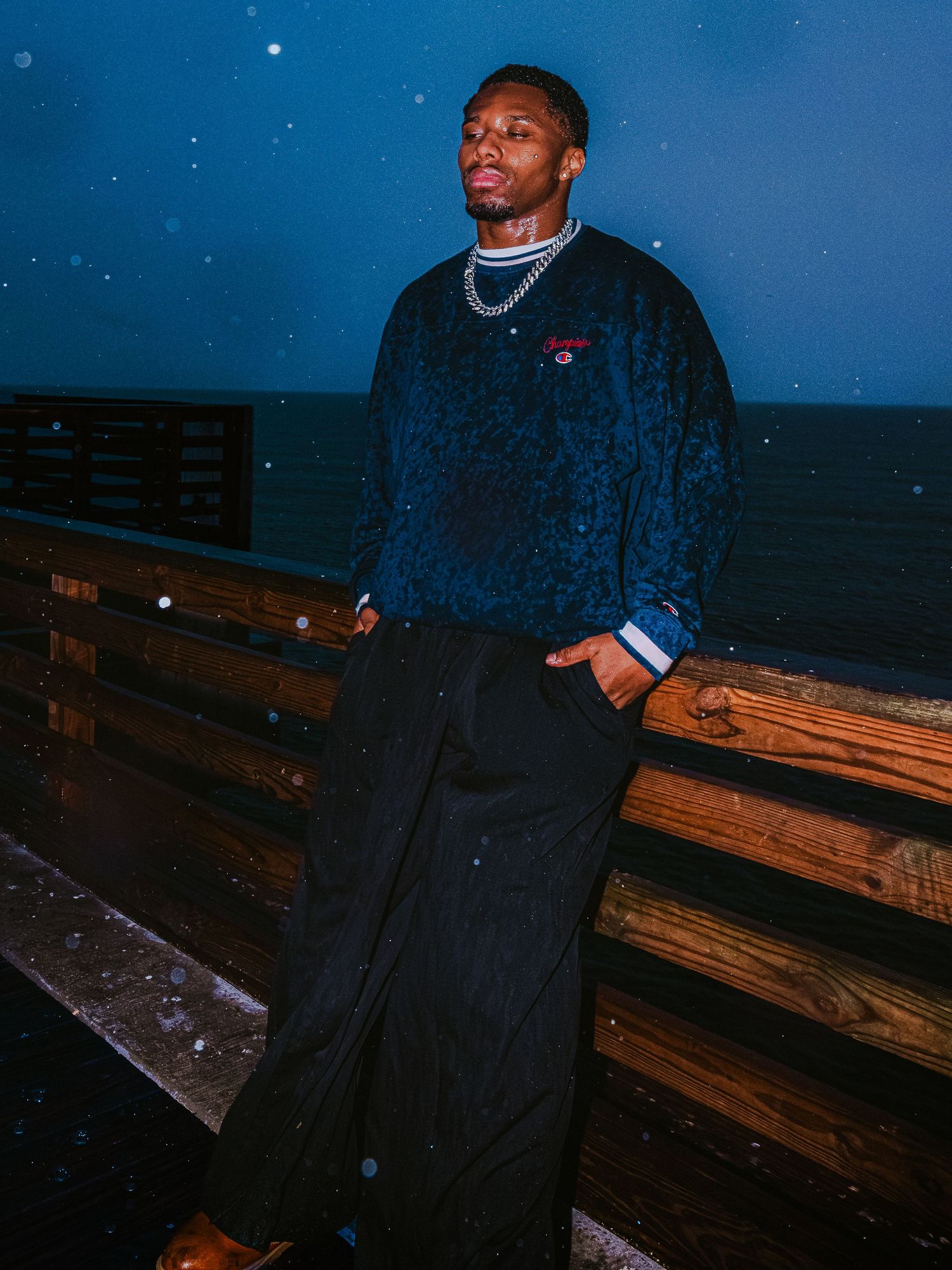 Portrait of person in dark sweater standing against wooden pier at night.