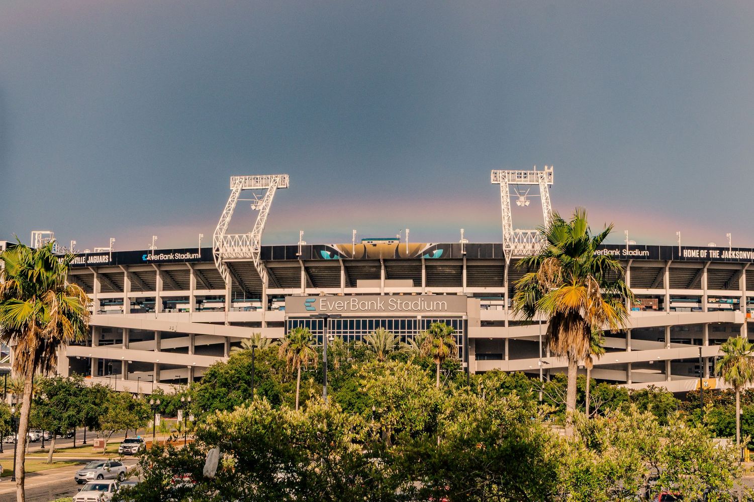 Stadium exterior view with palm trees and lighting structures during sunset.