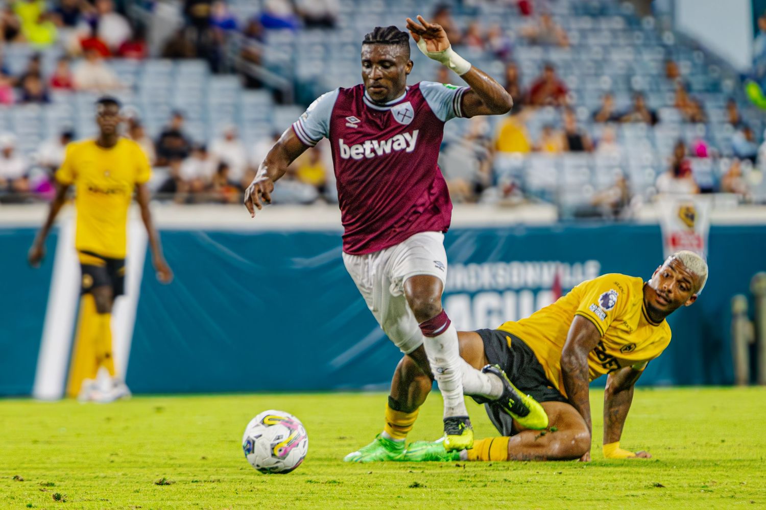 Soccer player dribbling past fallen defender during competitive match.