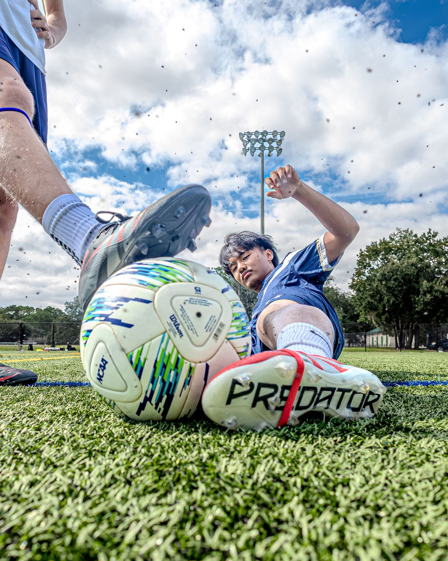 Soccer player slides for the ball on artificial turf under bright blue sky.