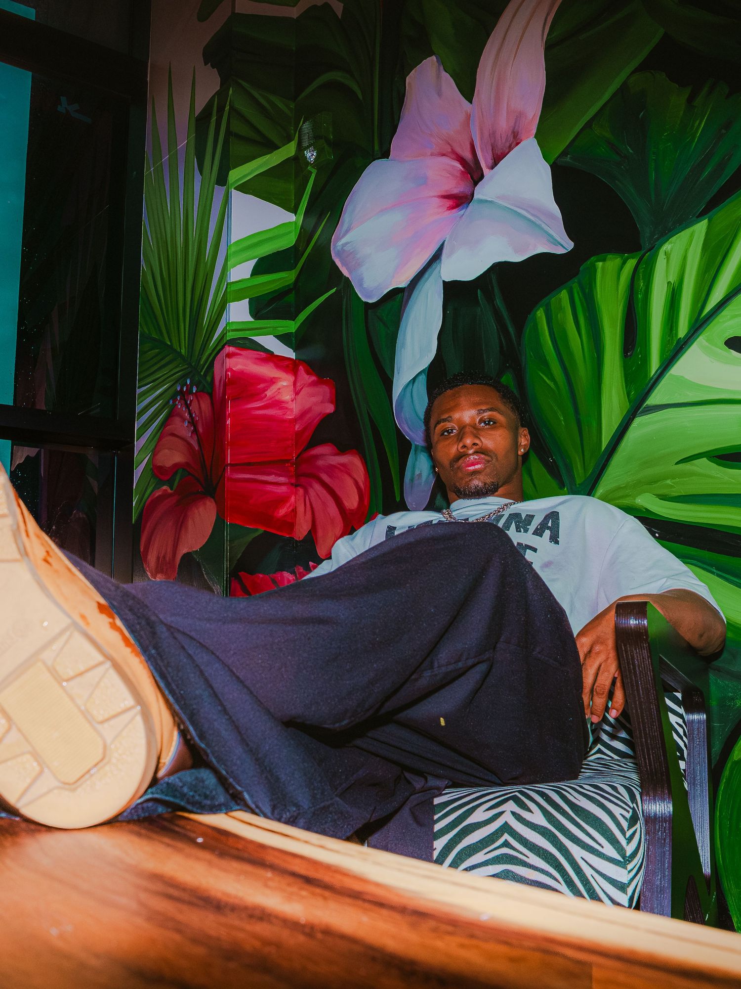 Artistic portrait against a tropical backdrop with green leaves and pink flowers.