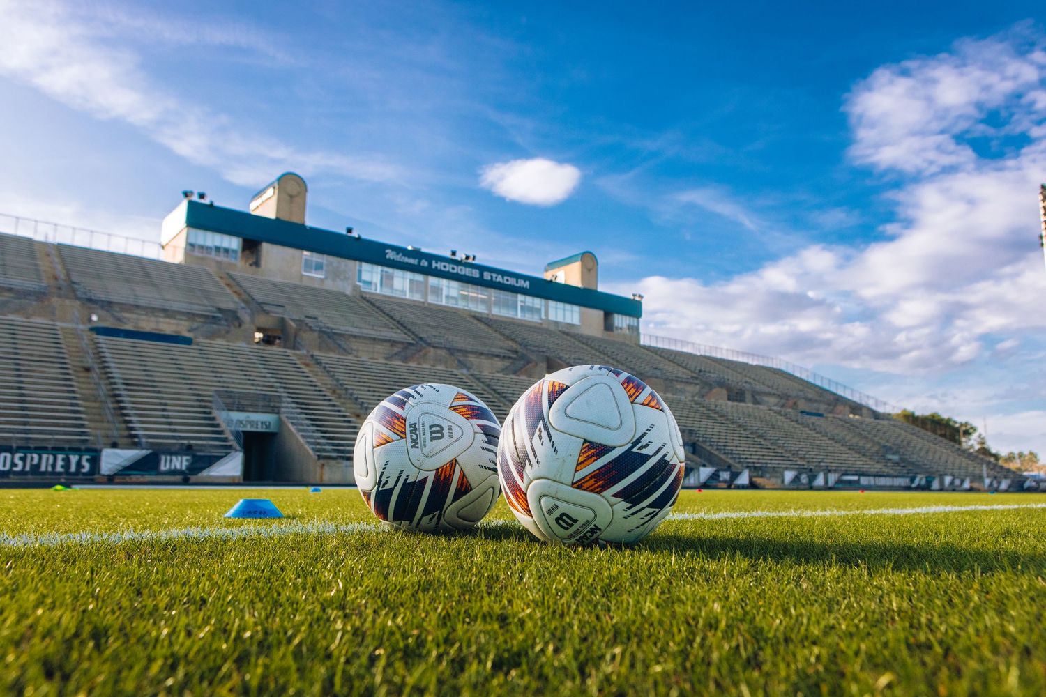 Football stadium bleachers and field under bright blue sky with scattered clouds.
