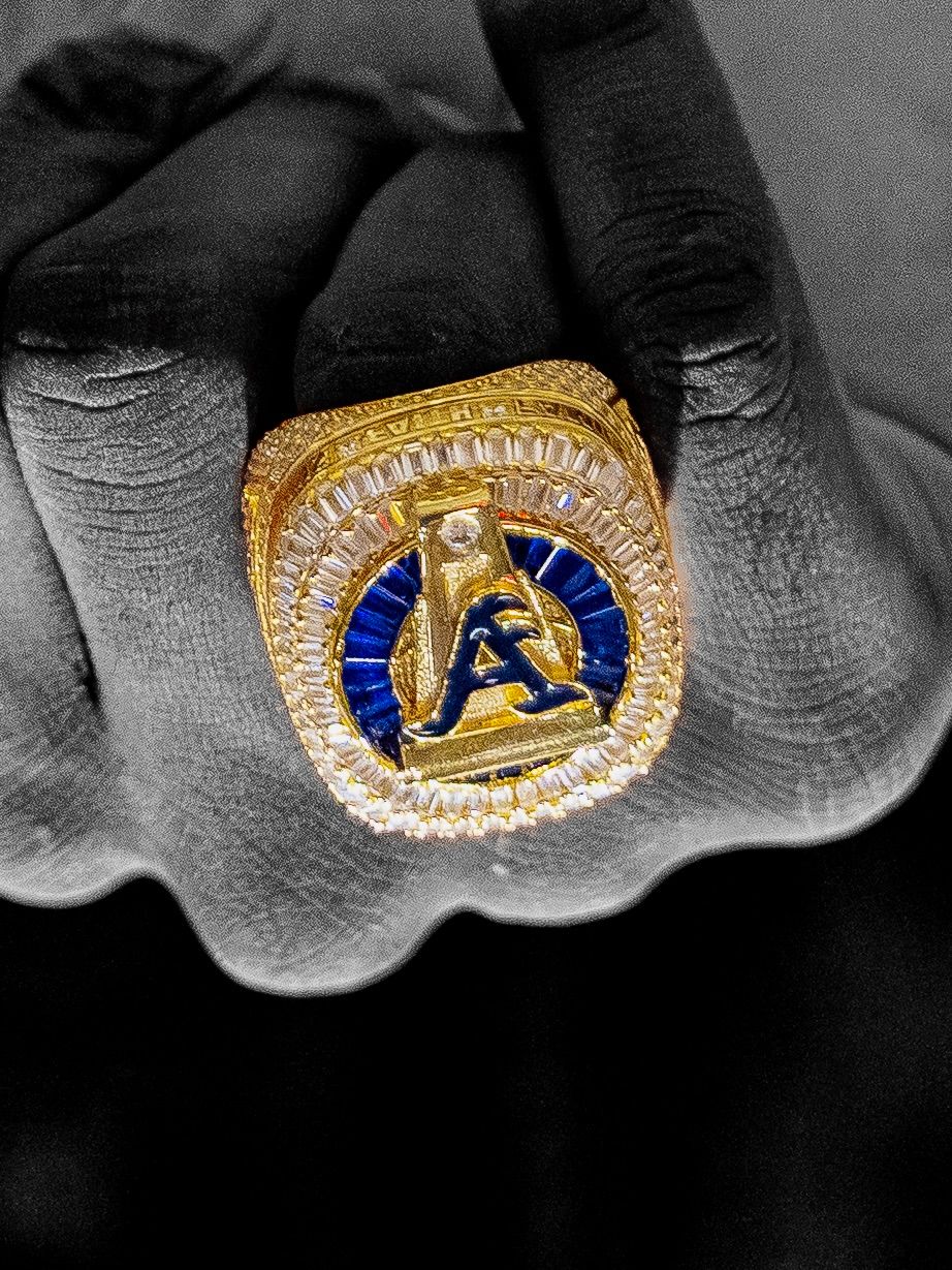 Championship ring with blue and gold design featuring athletic figure in center surrounded by diamonds.