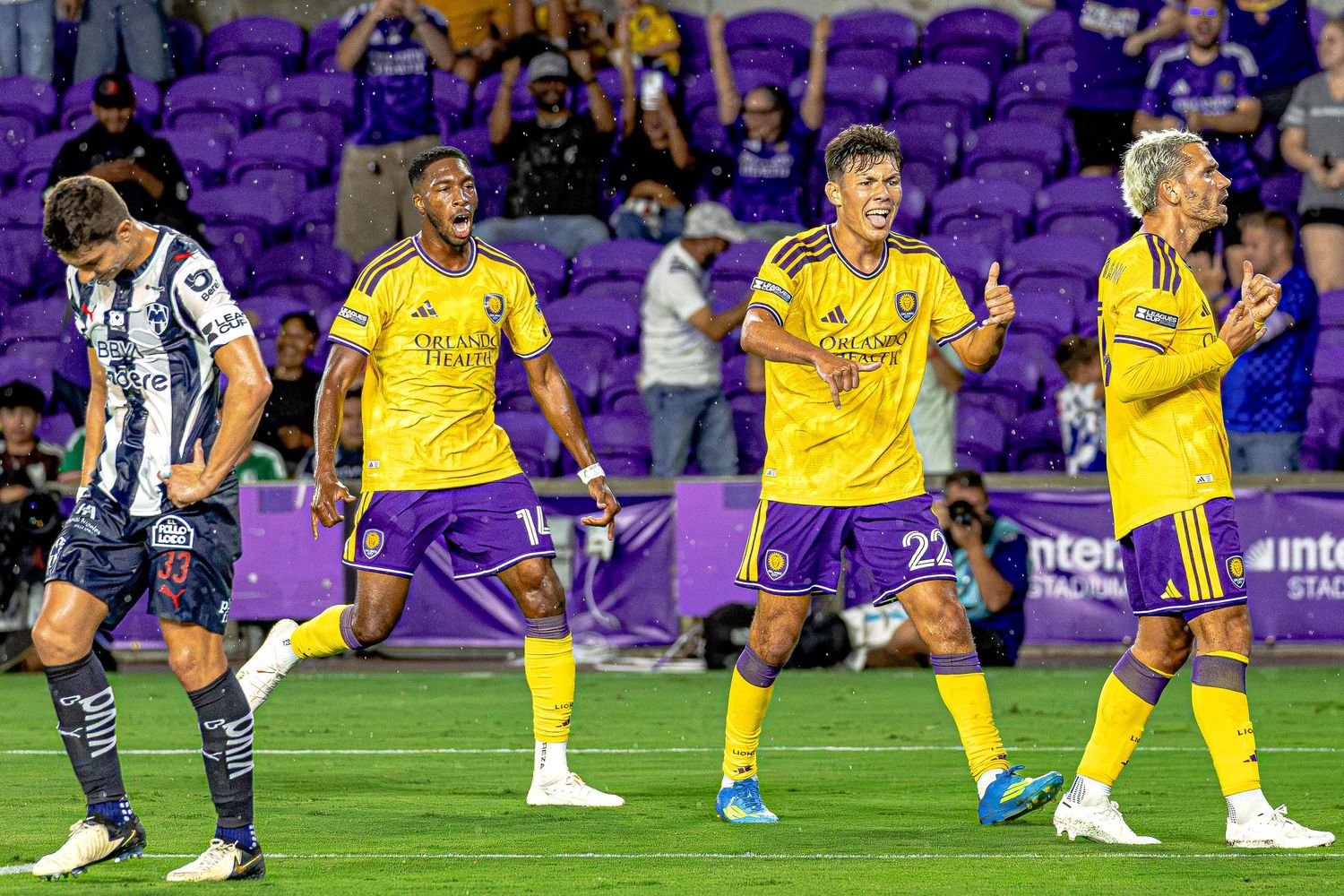 Orlando City SC players celebrate a goal in purple and yellow uniforms during an MLS soccer match at Exploria Stadium.