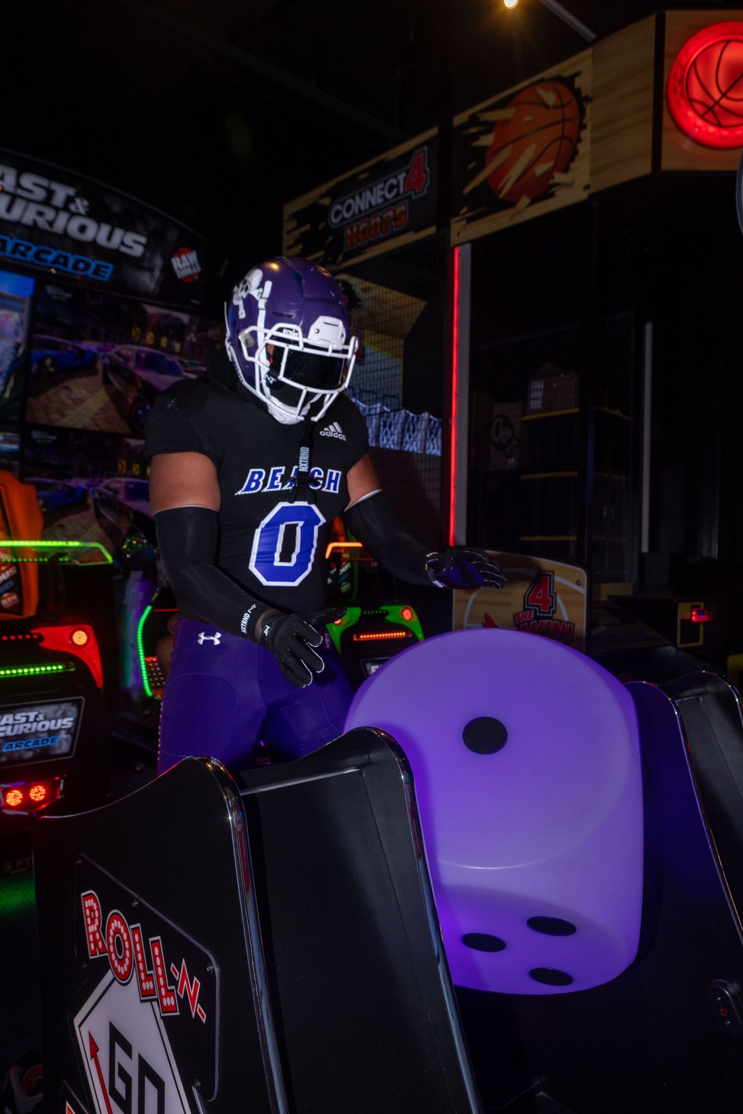 Arcade gaming setup with purple and black chairs illuminated by neon lights in a dark room.