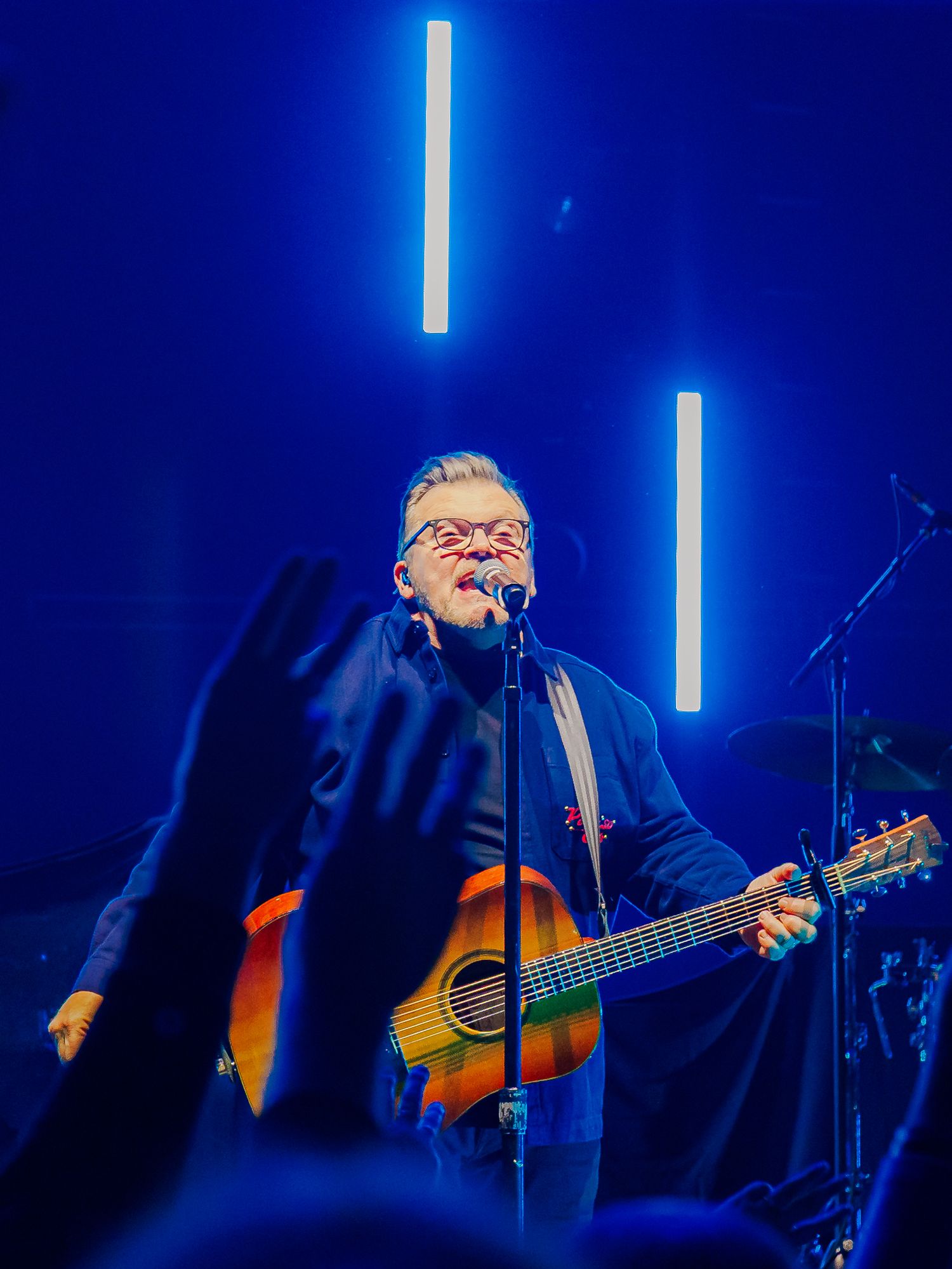 Musician performing with acoustic guitar against blue stage lighting.