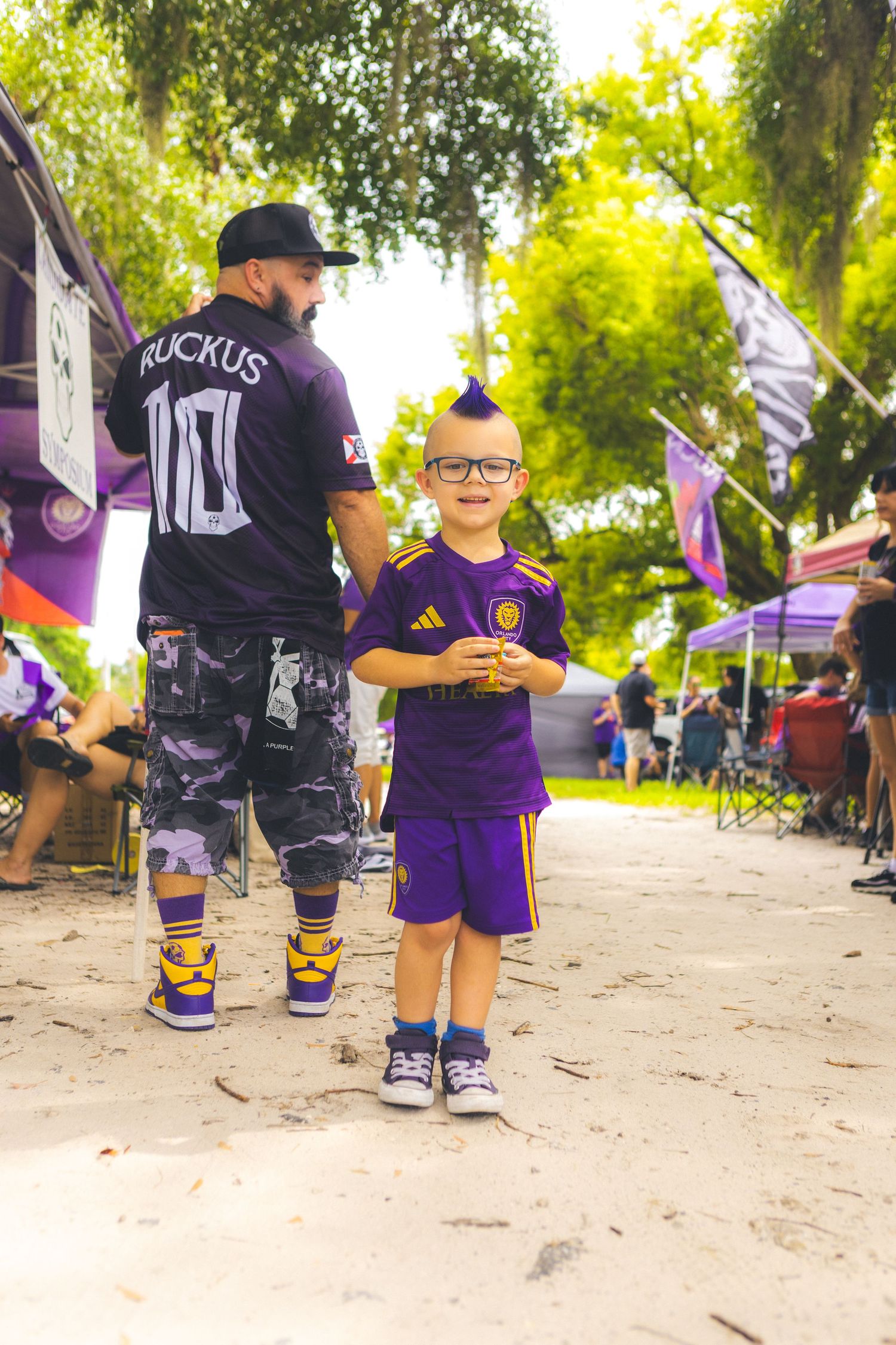 Group of soccer fans in purple team gear gather outdoors on a sunny day.