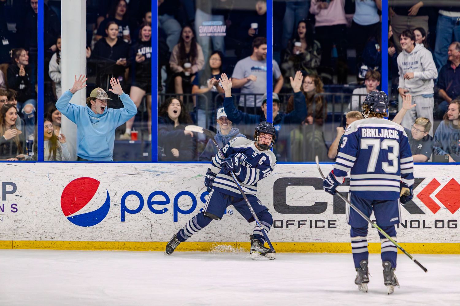 Hockey players in action on ice rink with stadium advertisements visible in background.