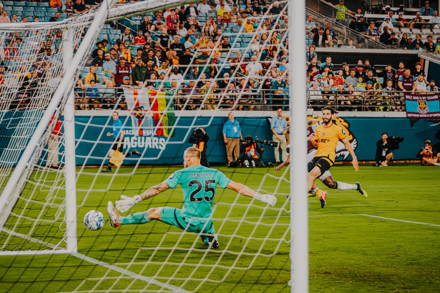 Soccer goalkeeper diving to make save during match with goal post visible.