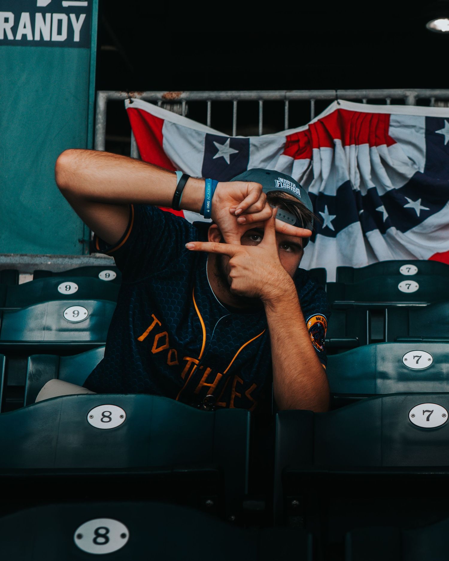 Baseball dugout with equipment and American flag bunting visible in the background.