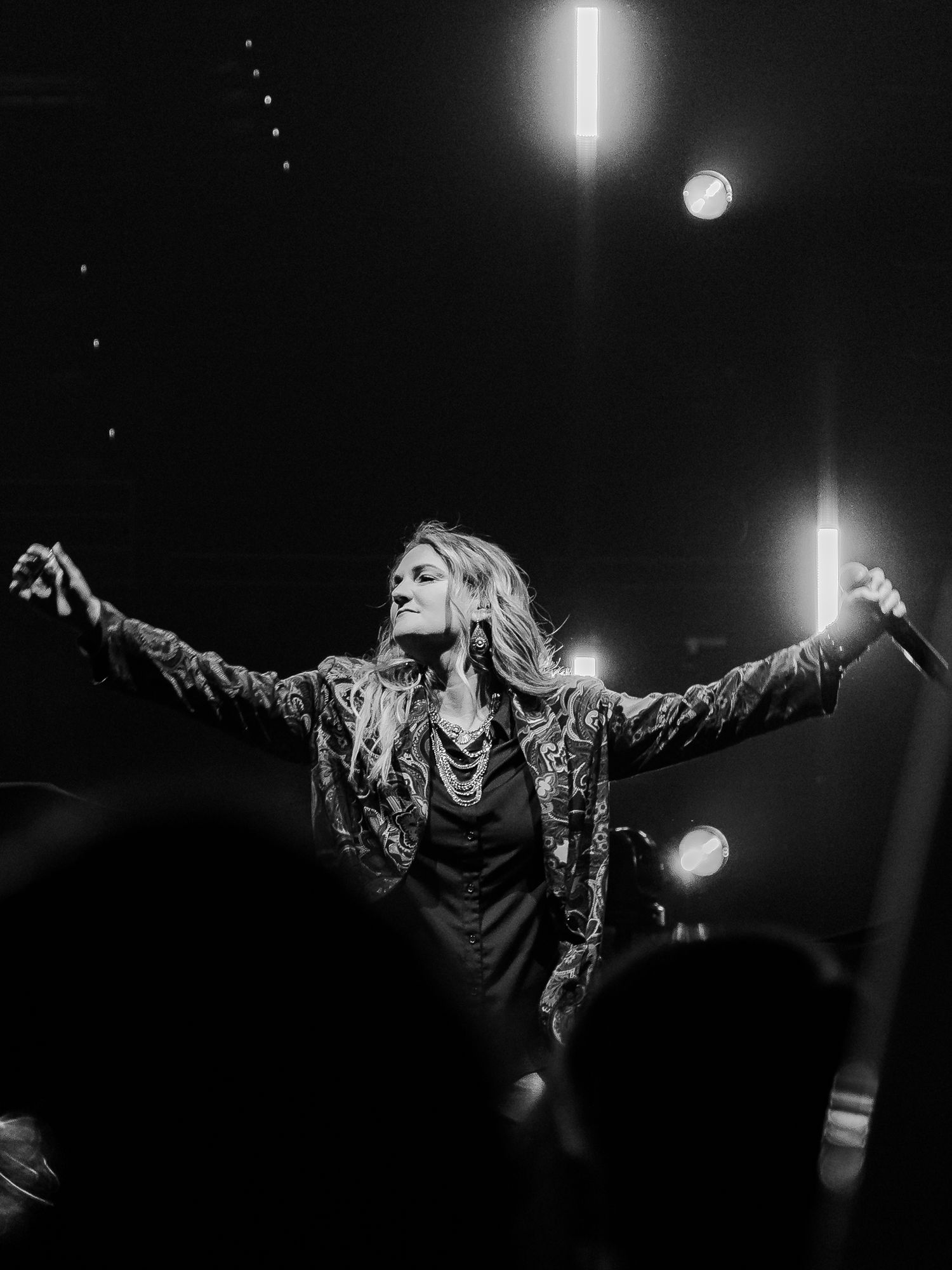 Performer with outstretched arms on stage under dramatic spotlighting.