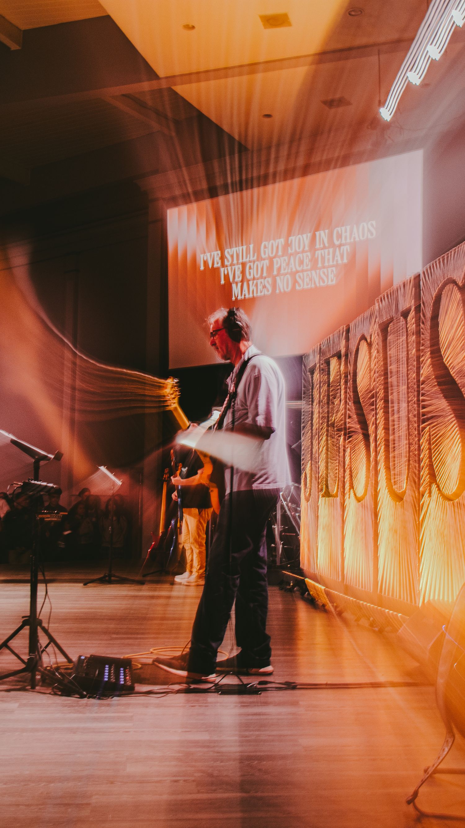 Performance art installation with dramatic orange lighting and text projections on walls.