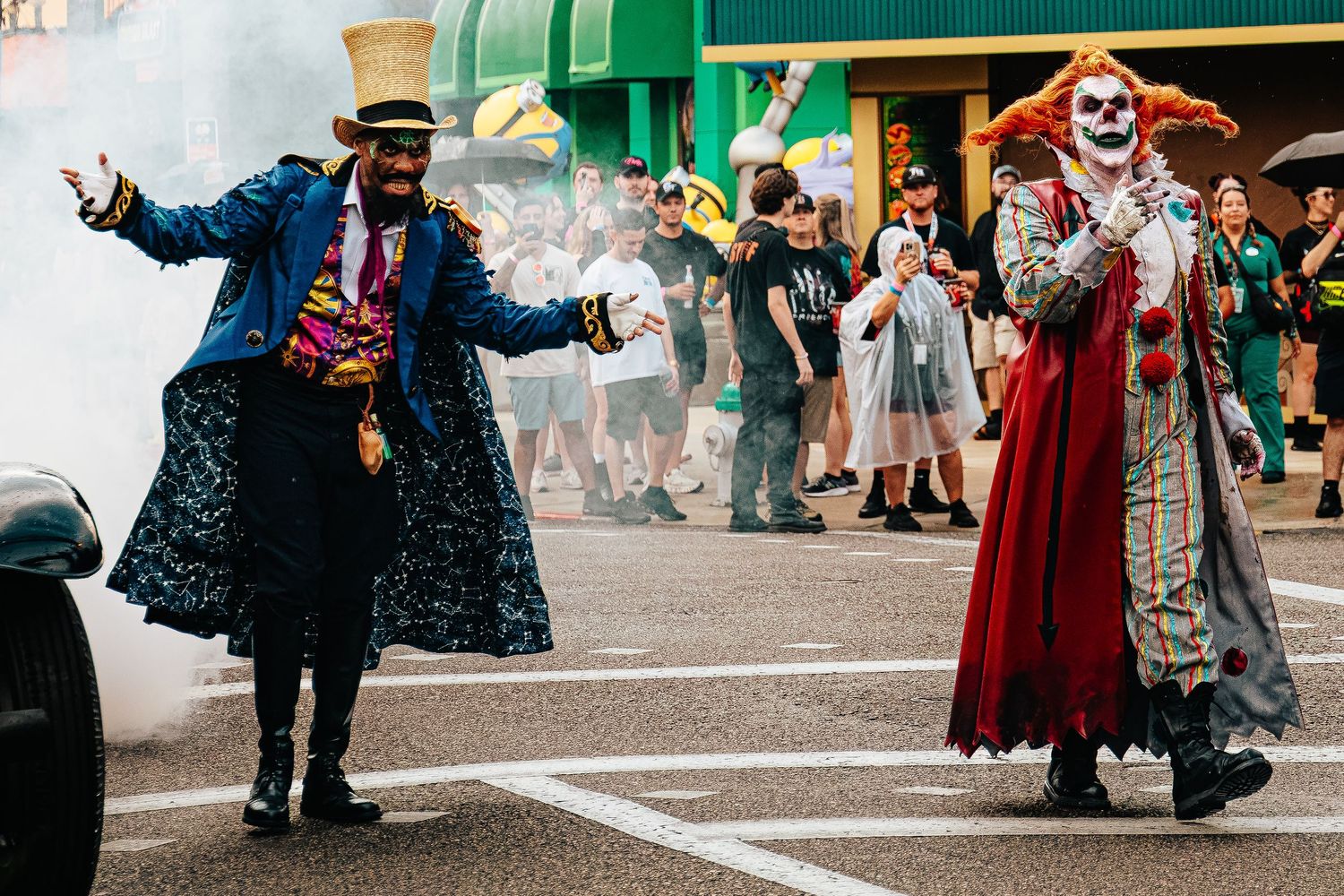 Two costumed performers in spooky clown and ringmaster outfits entertain crowds at a Halloween street parade.