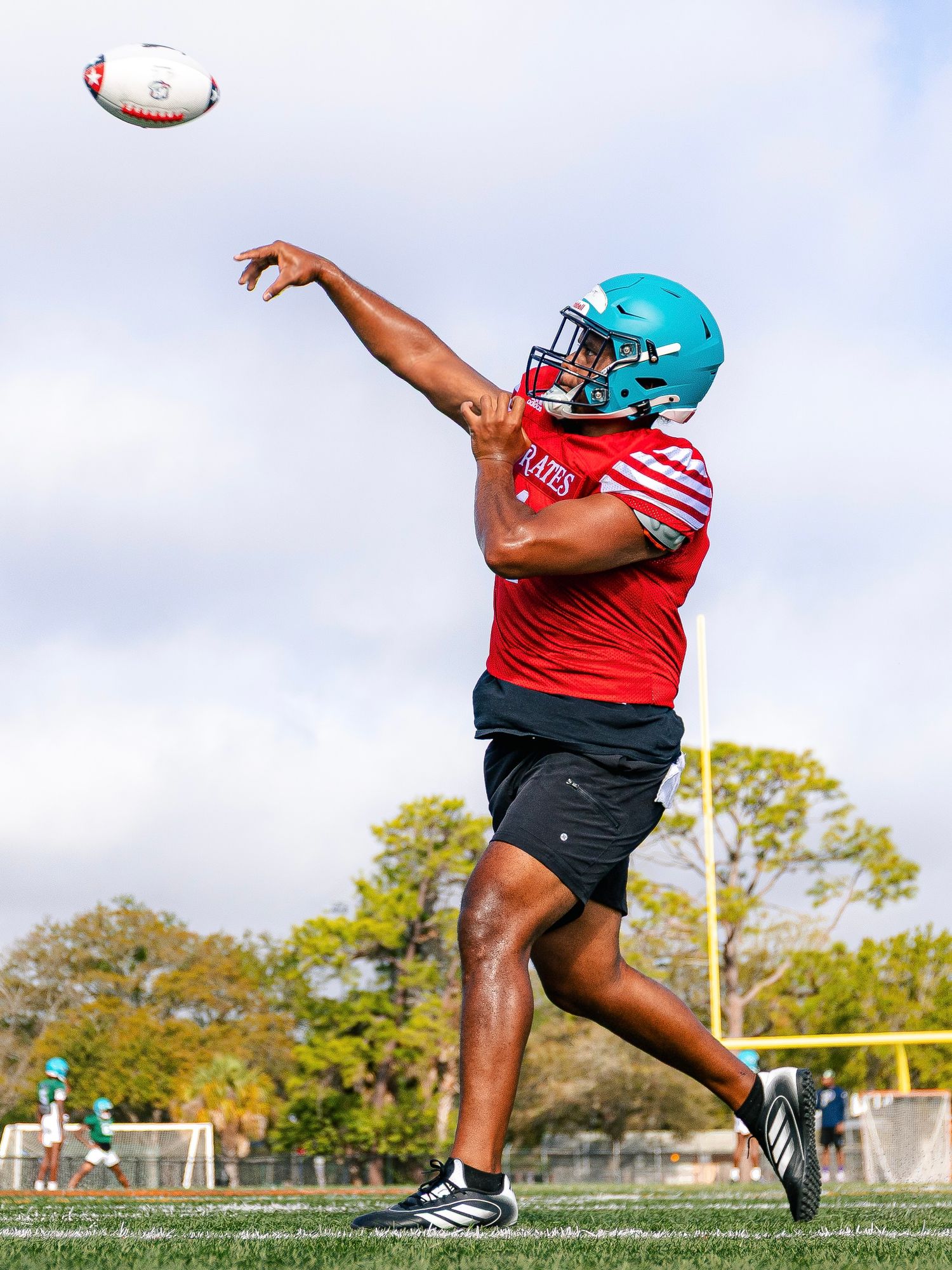 Football player in teal and red uniform throwing ball during practice session.