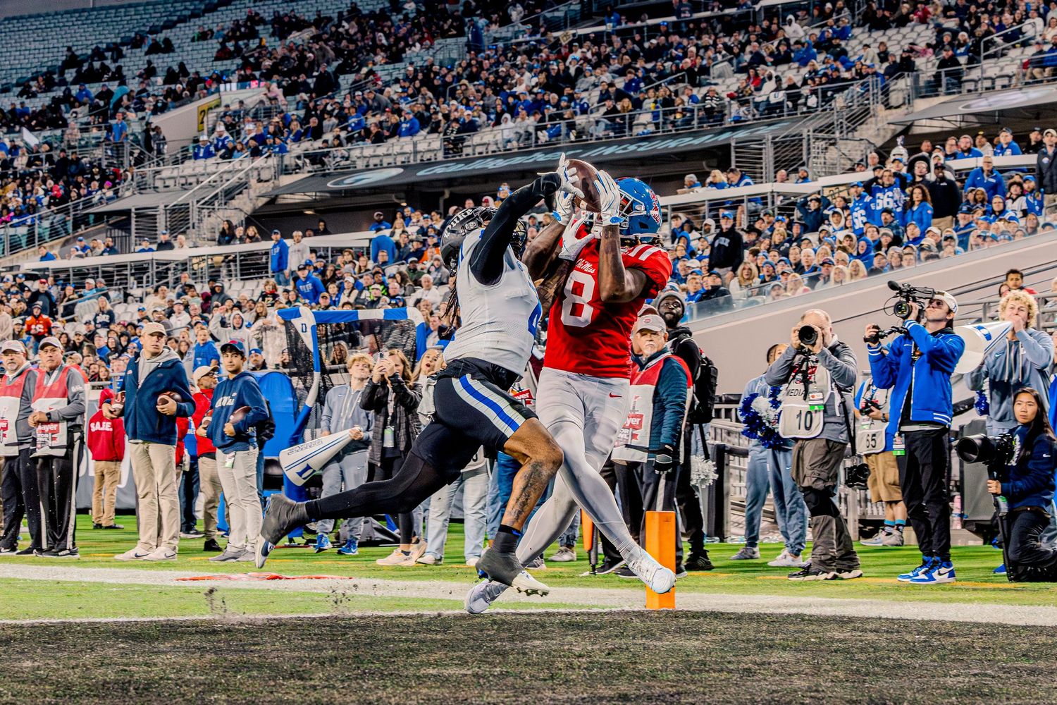 Wide angle view of football game action with spectators in stadium stands.