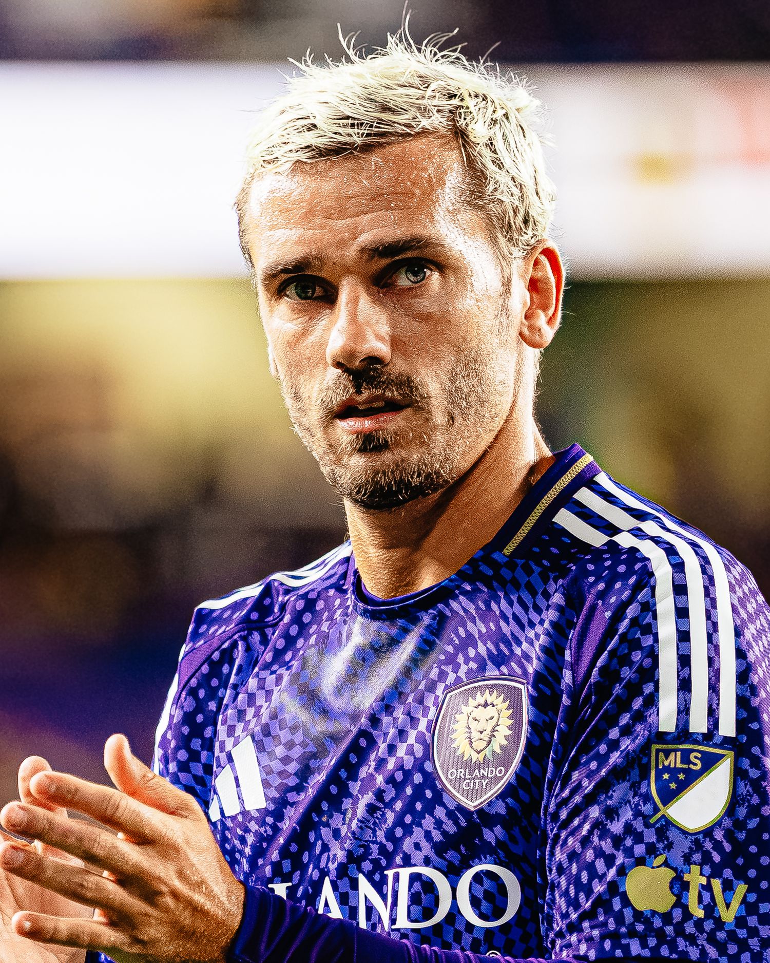 Orlando City SC soccer player in purple MLS jersey applauding on the field during a night match.