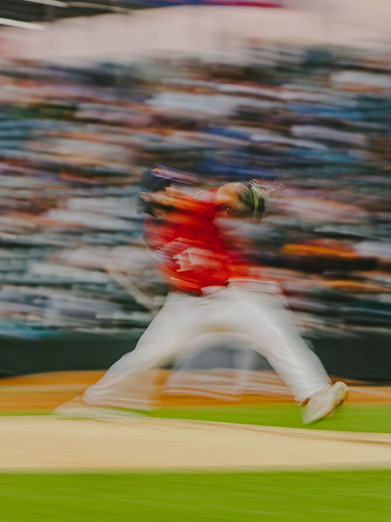 Motion blurred baseball pitcher in white uniform throwing pitch on field.