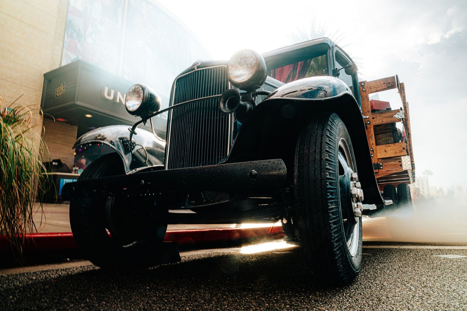 Vintage black antique car with round headlights photographed from low angle, surrounded by atmospheric smoke at a classic car show.