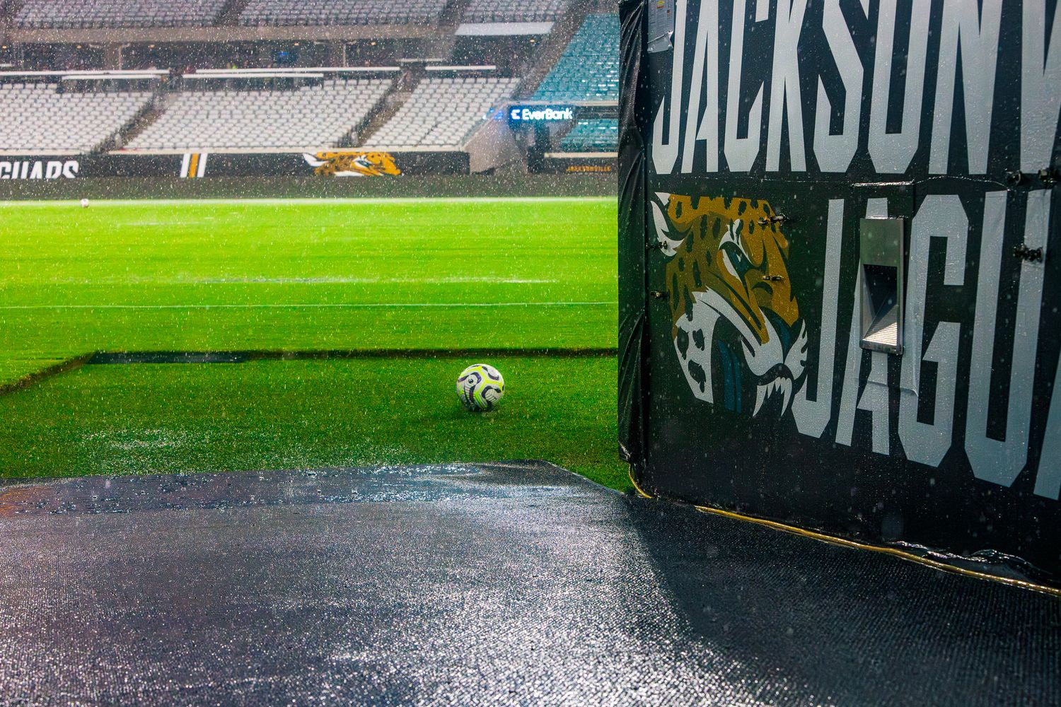Wet football field with green turf and stadium signage visible along sideline.