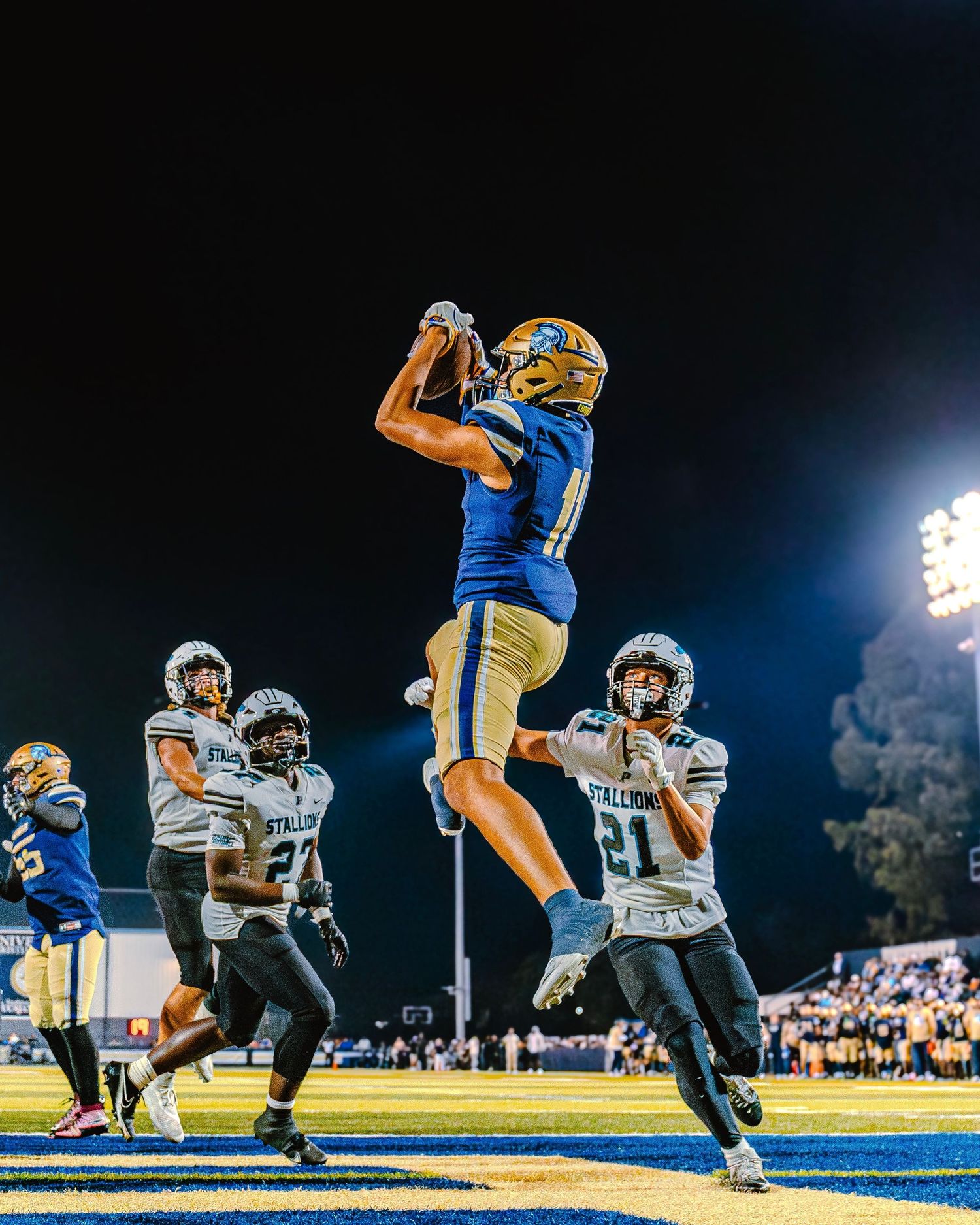 Football players in blue and white uniforms competing during nighttime game under stadium lights.