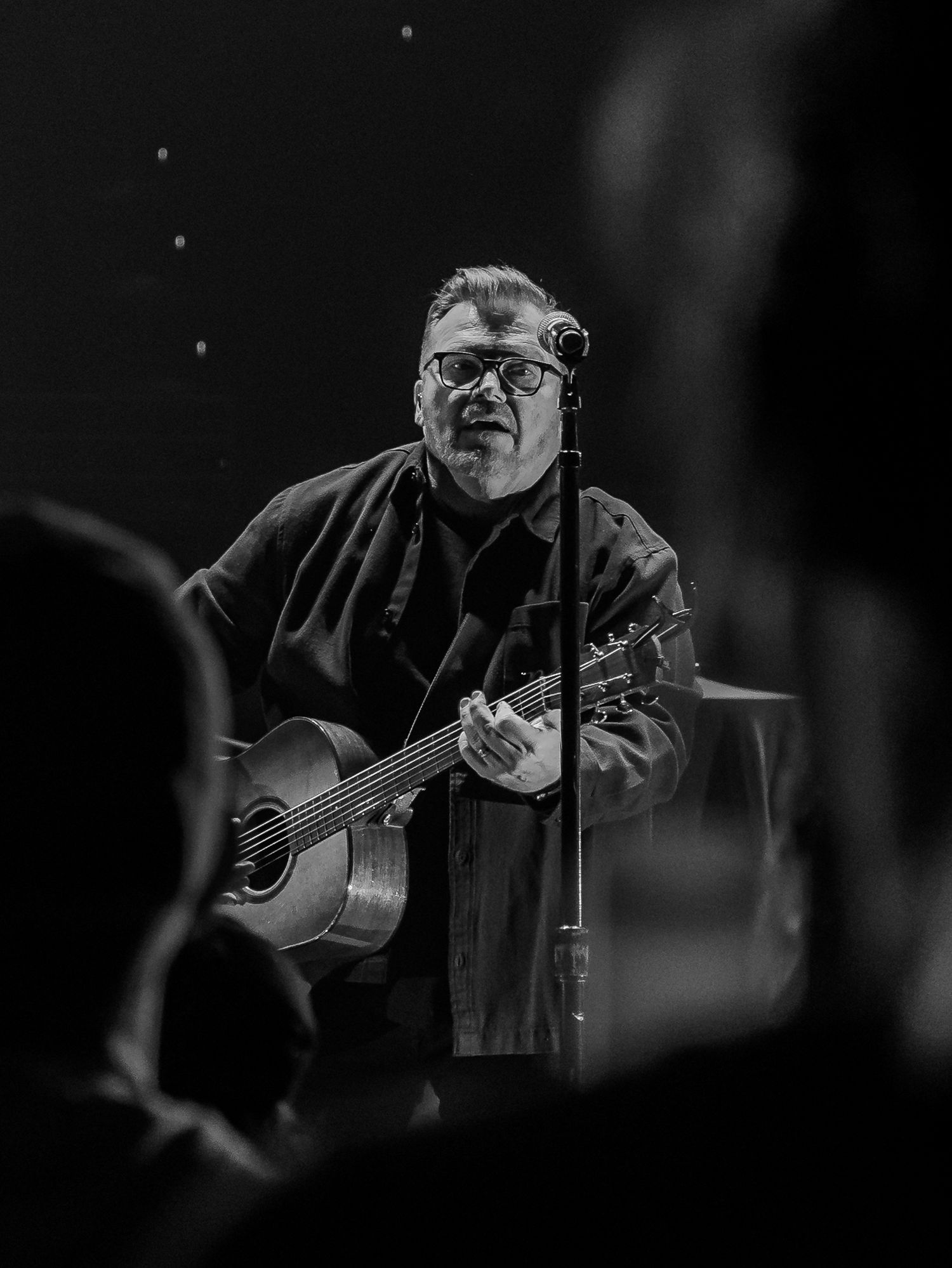 Close-up of musician playing acoustic guitar in moody black and white lighting.