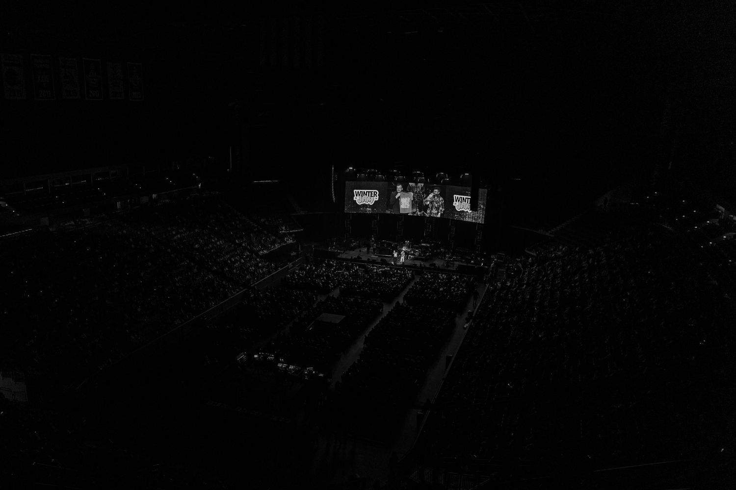 Dark concert venue with stage lighting and crowd silhouettes.