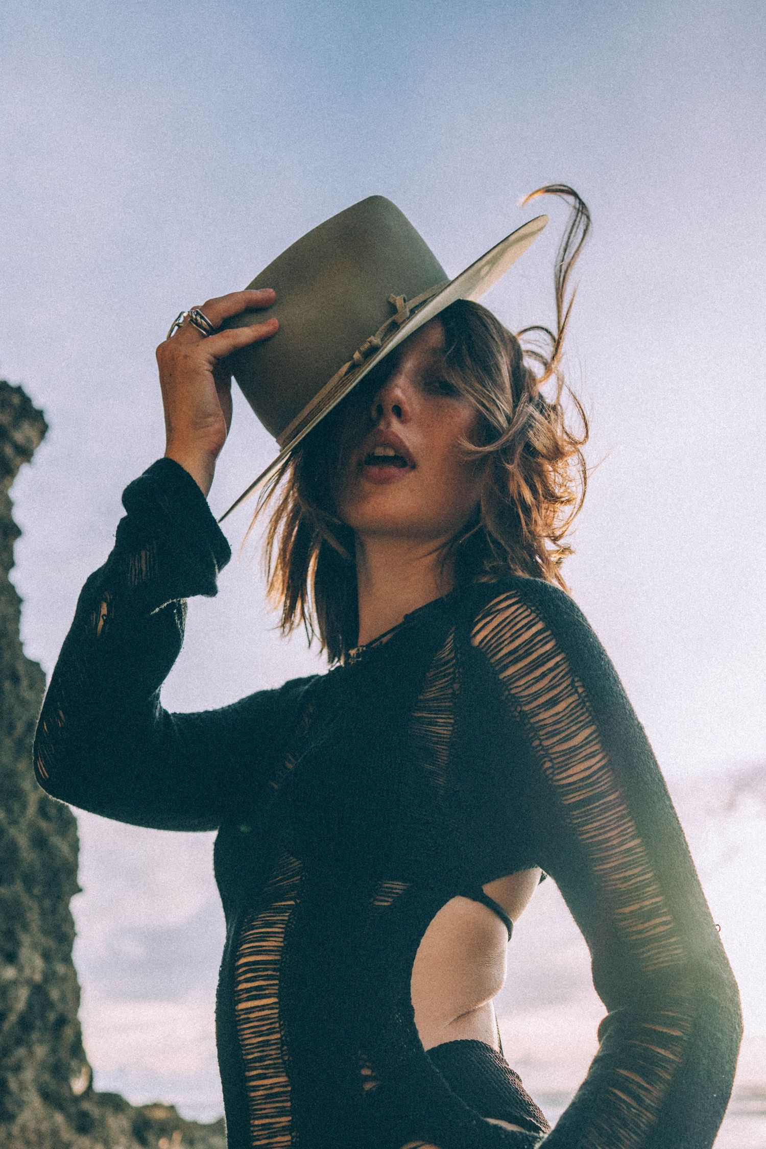 Woman adjusting wide-brim hat outdoors in natural light.