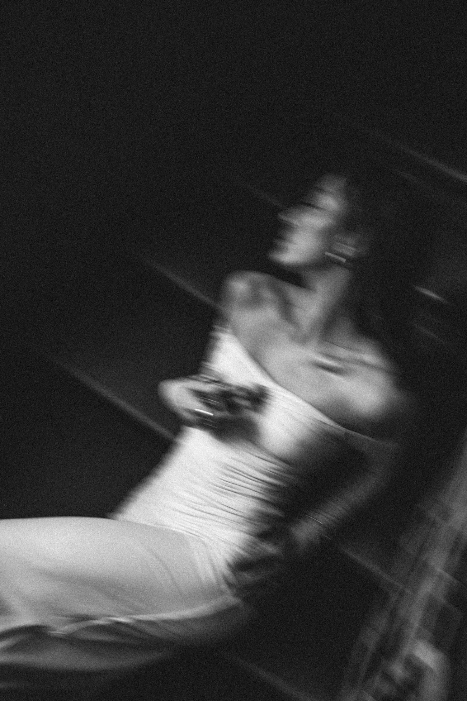 Black and white motion-blurred portrait of woman seated in low light.