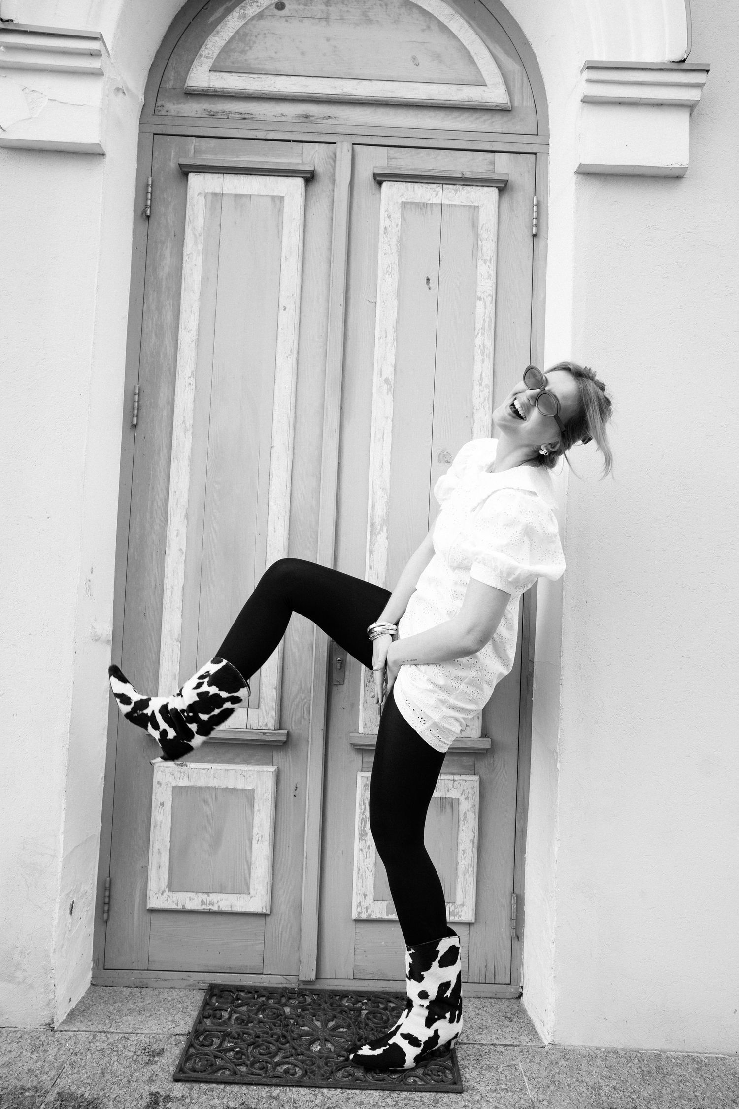 Black and white fashion portrait of woman posing playfully against vintage doorway