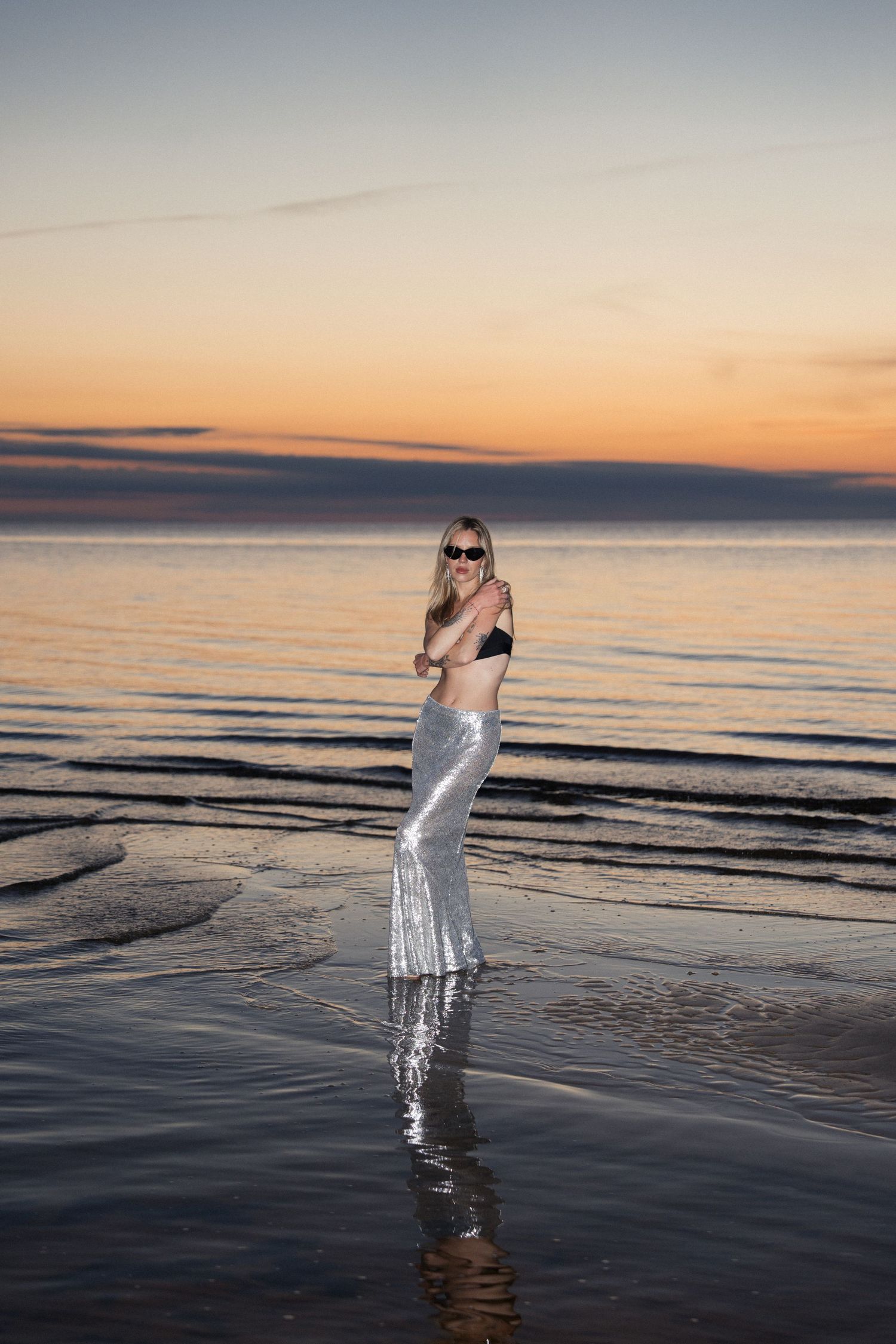 Woman standing in shallow ocean water during calm sunset light