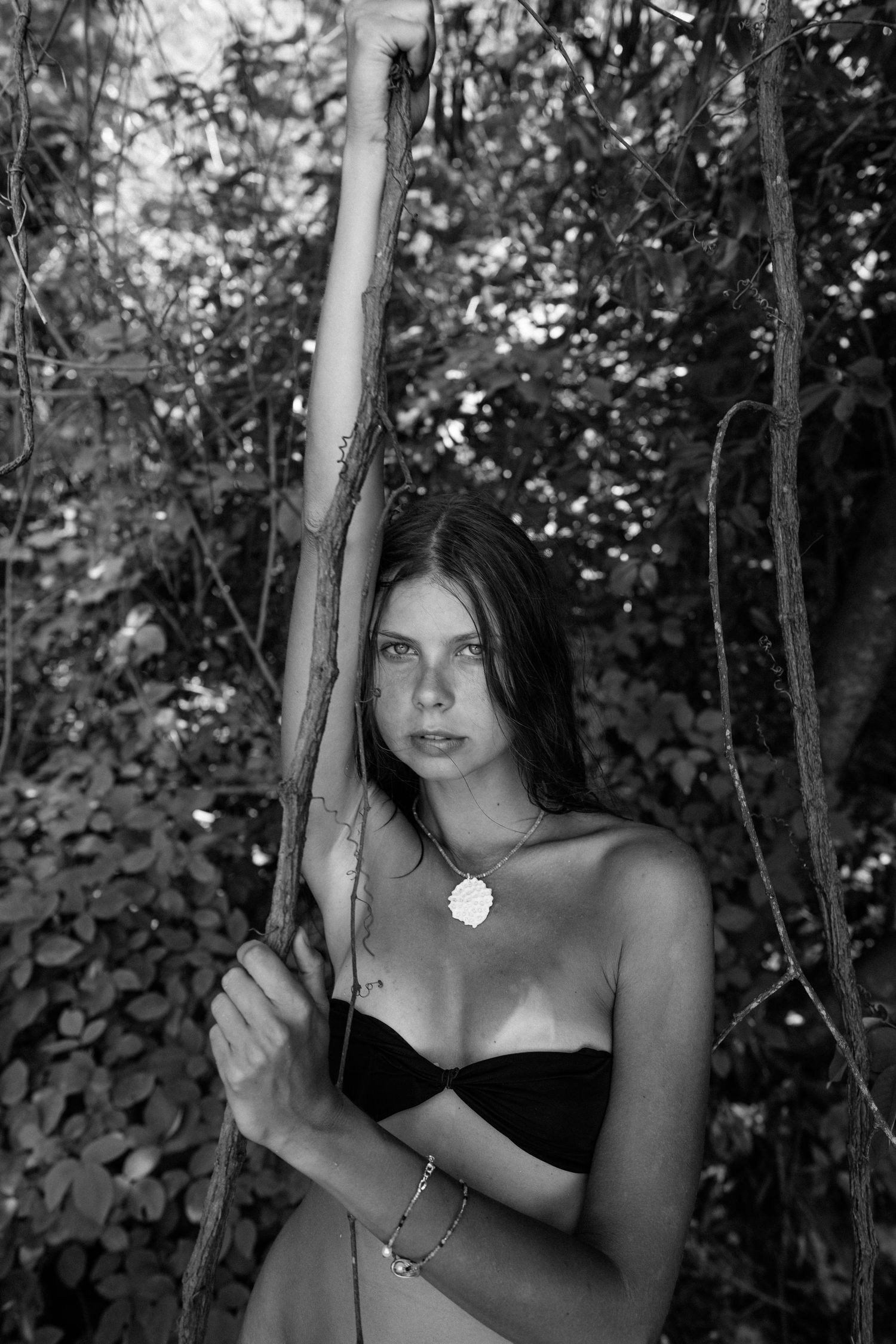 Black and white portrait of woman holding slender tree branch in wooded setting.