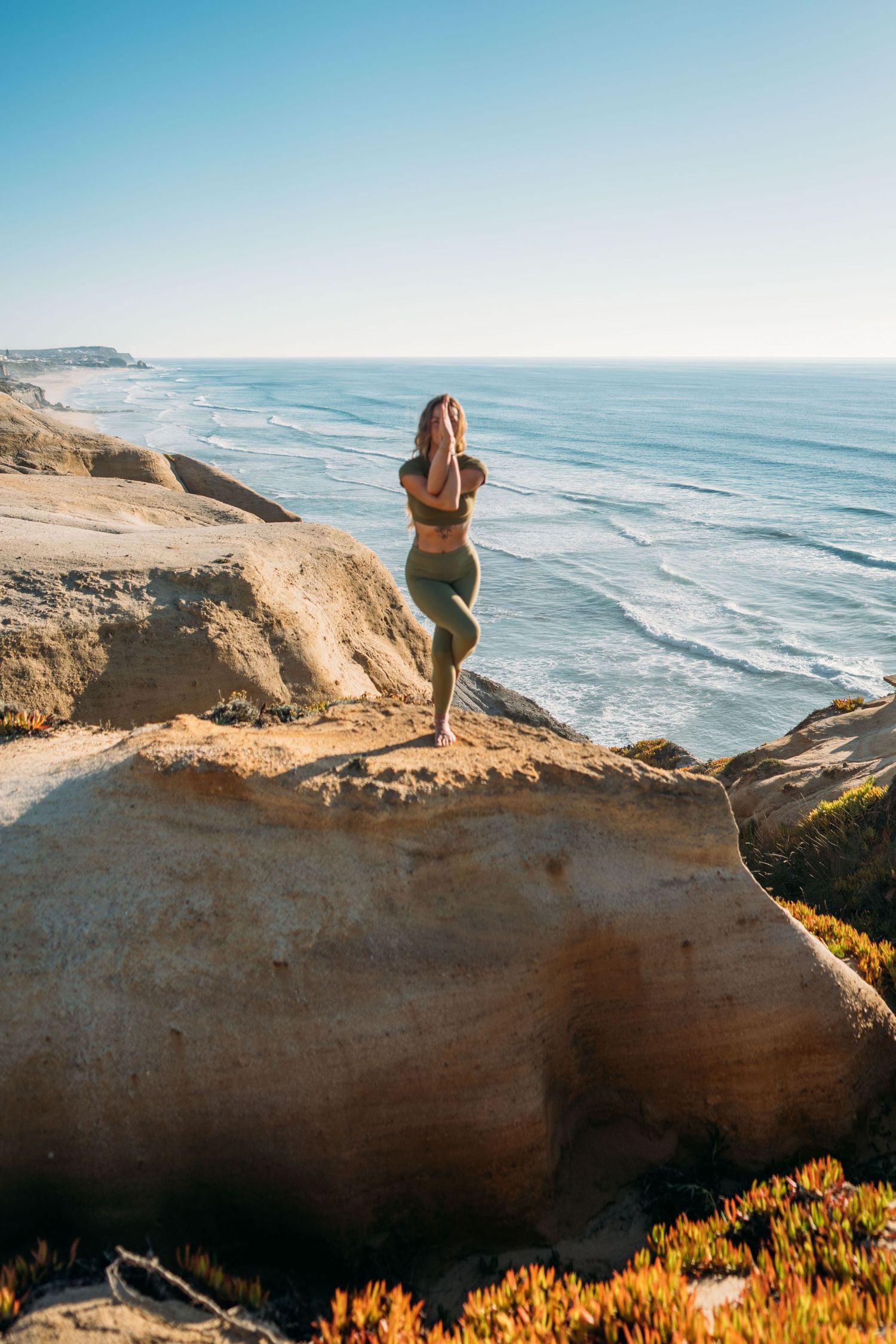 Woman standing on coastal cliff overlooking the ocean in clear daylight.