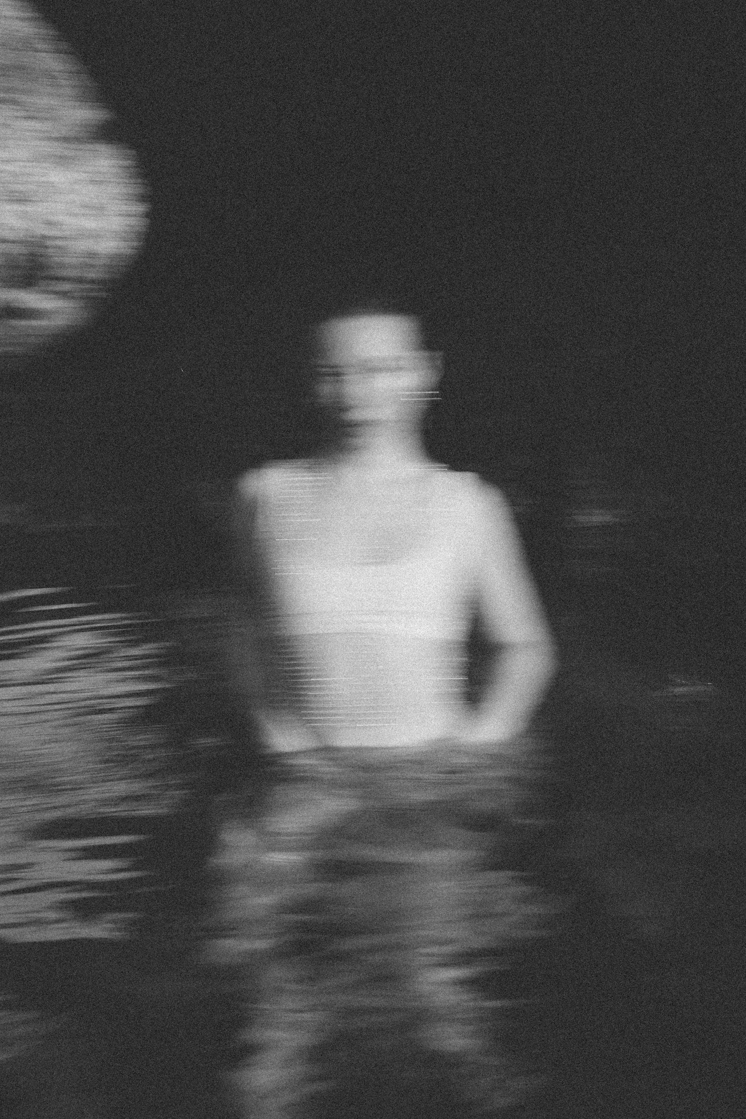 Black and white motion-blurred portrait of woman standing in shallow water.