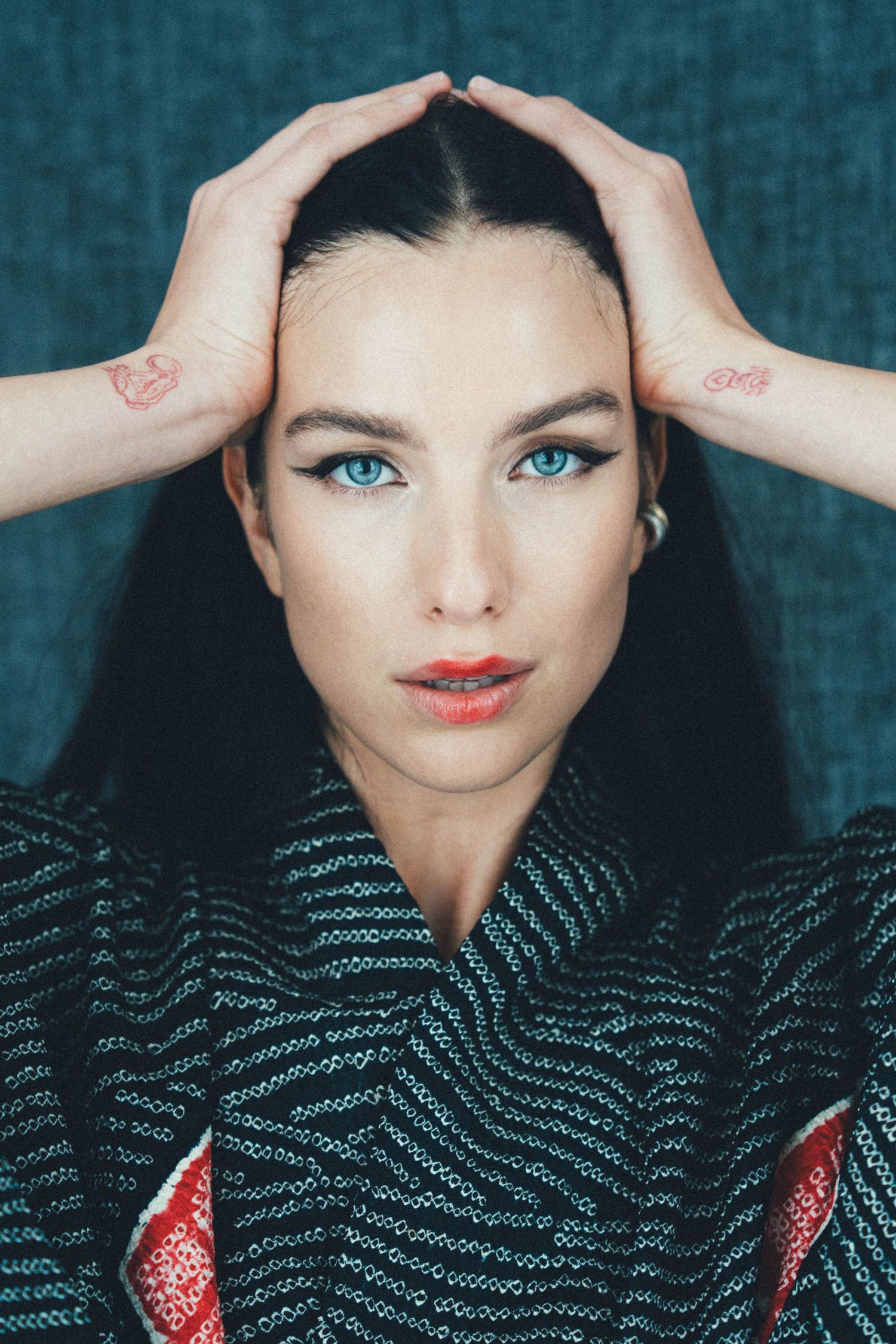 Close-up portrait of woman with hands resting on head against dark background.