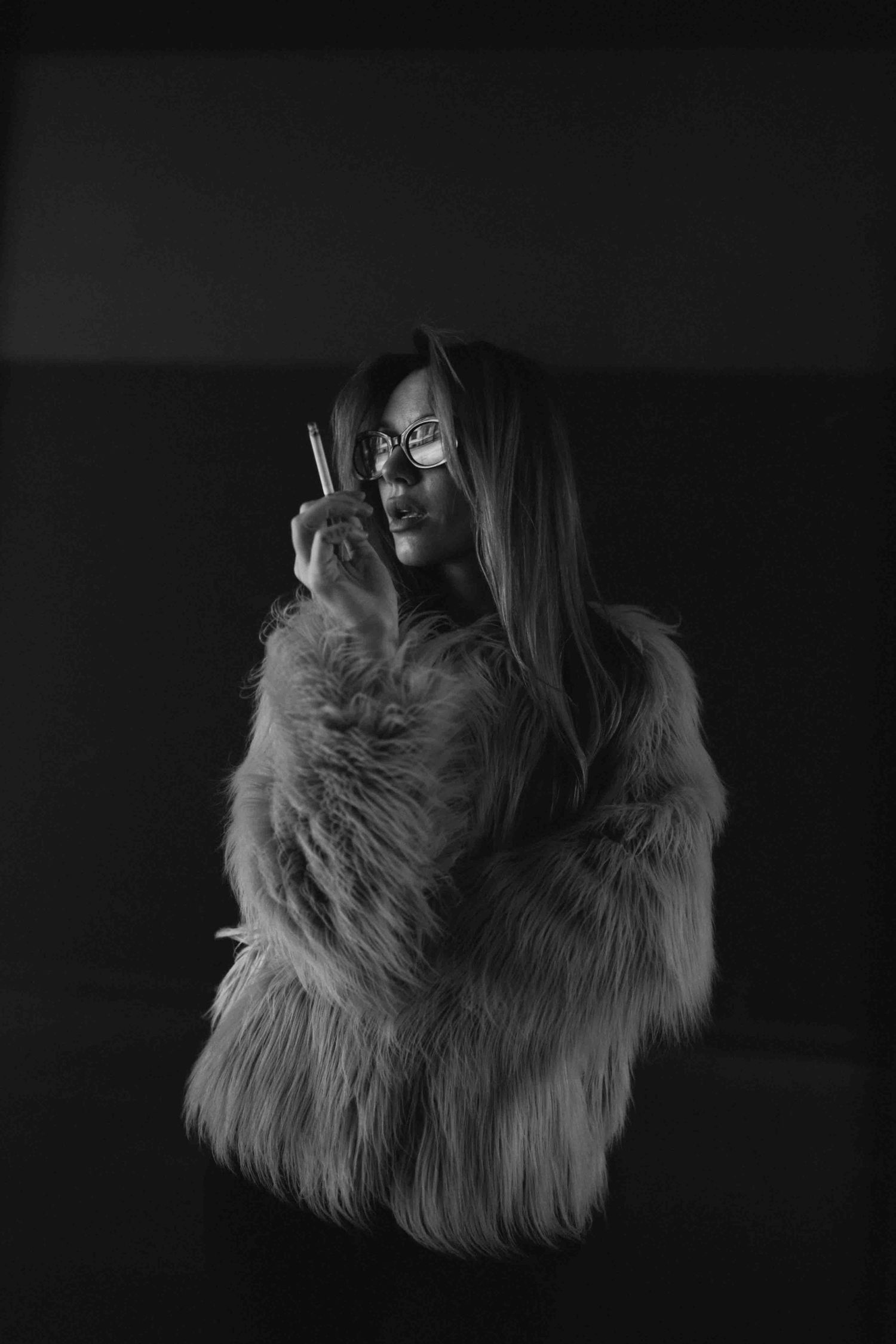 Black and white portrait of woman wearing textured fur coat in low light.